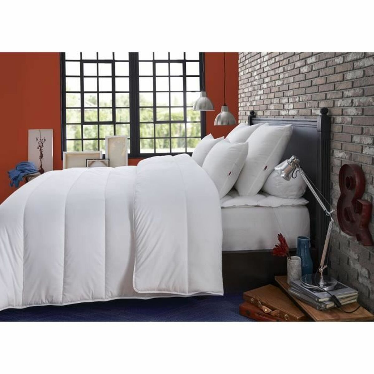 Weiße Bettwäsche auf einem Bett, mit Fenster, Backsteinmauer und Lampe im Hintergrund.
