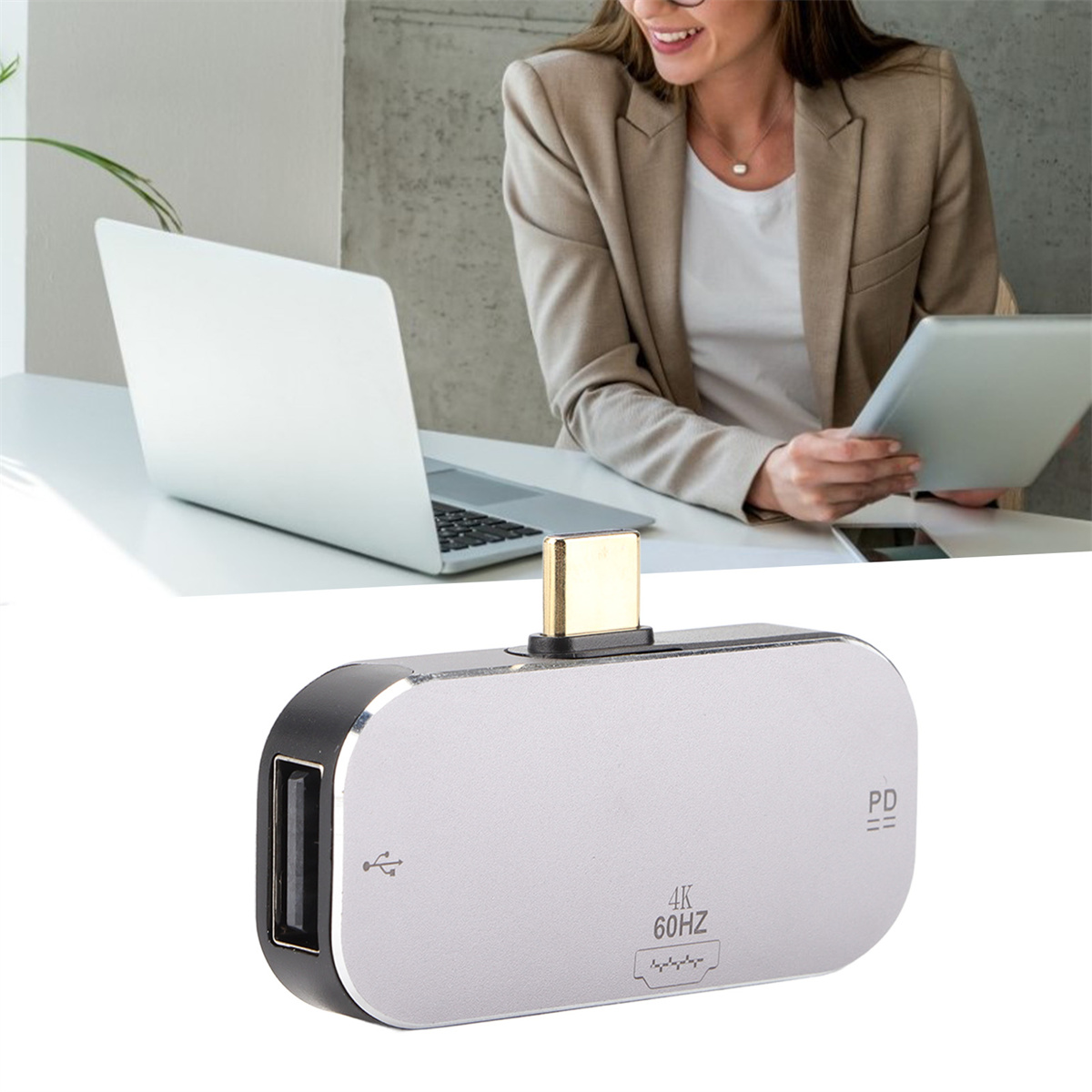 Silberner USB-C-Hub mit USB-Anschluss und einer Frau, die an einem Laptop und Tablet arbeitet.