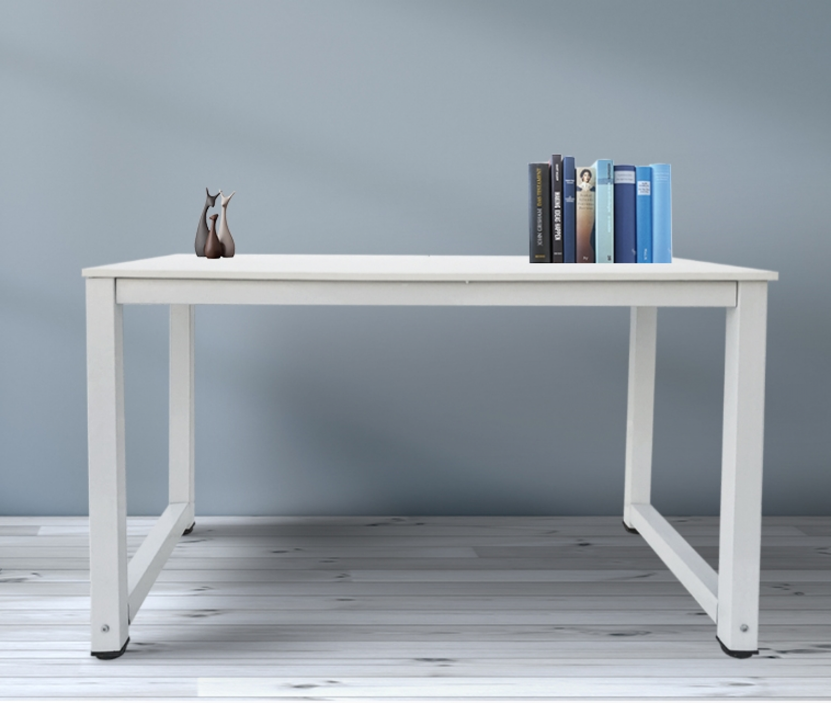 Weißer Schreibtisch mit Büchern und einer Skulptur. Blaue Wand im Hintergrund. Der Schreibtisch hat Metallrahmen.