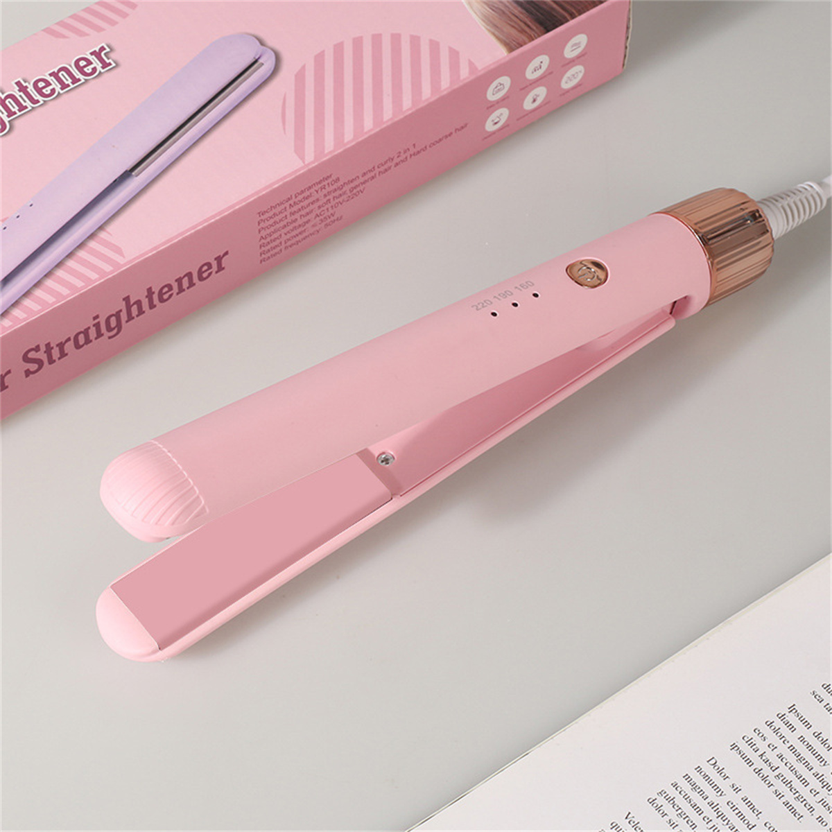 Rosa Glätteisen und rosa Box auf Tisch mit Buch.