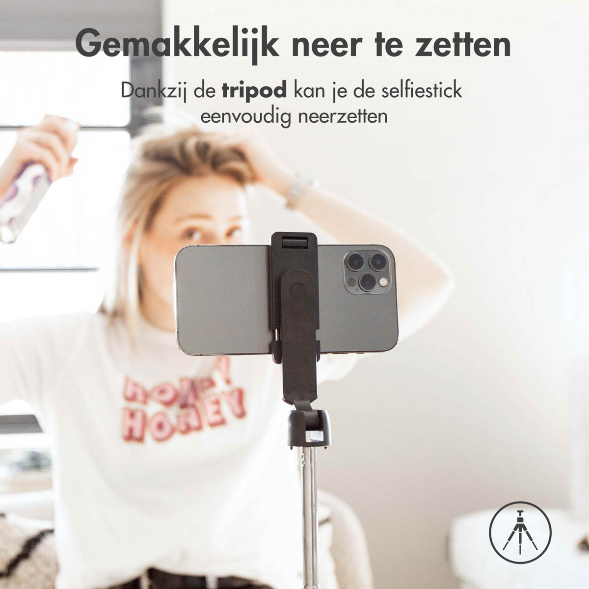 A woman holding a hair product and using a selfie stick with phone attached.