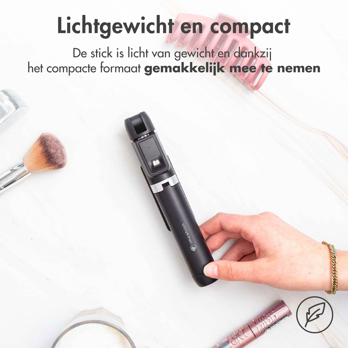 A person holding a selfie stick with makeup items in the background.
