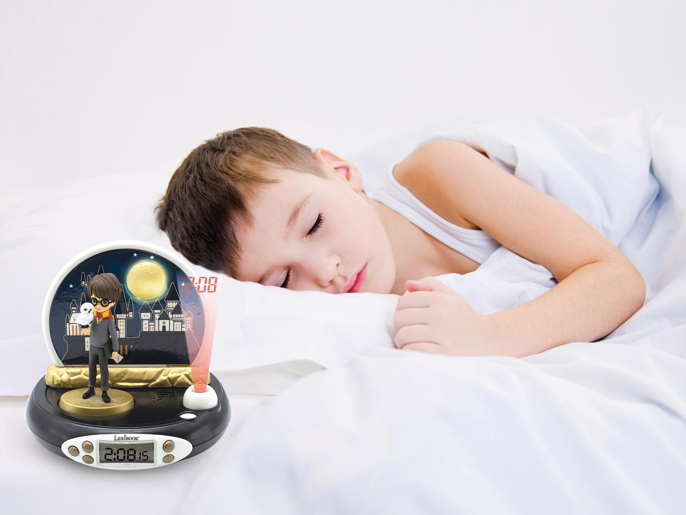 Un niño durmiendo en la cama junto a un despertador temático de Harry Potter que muestra la hora.