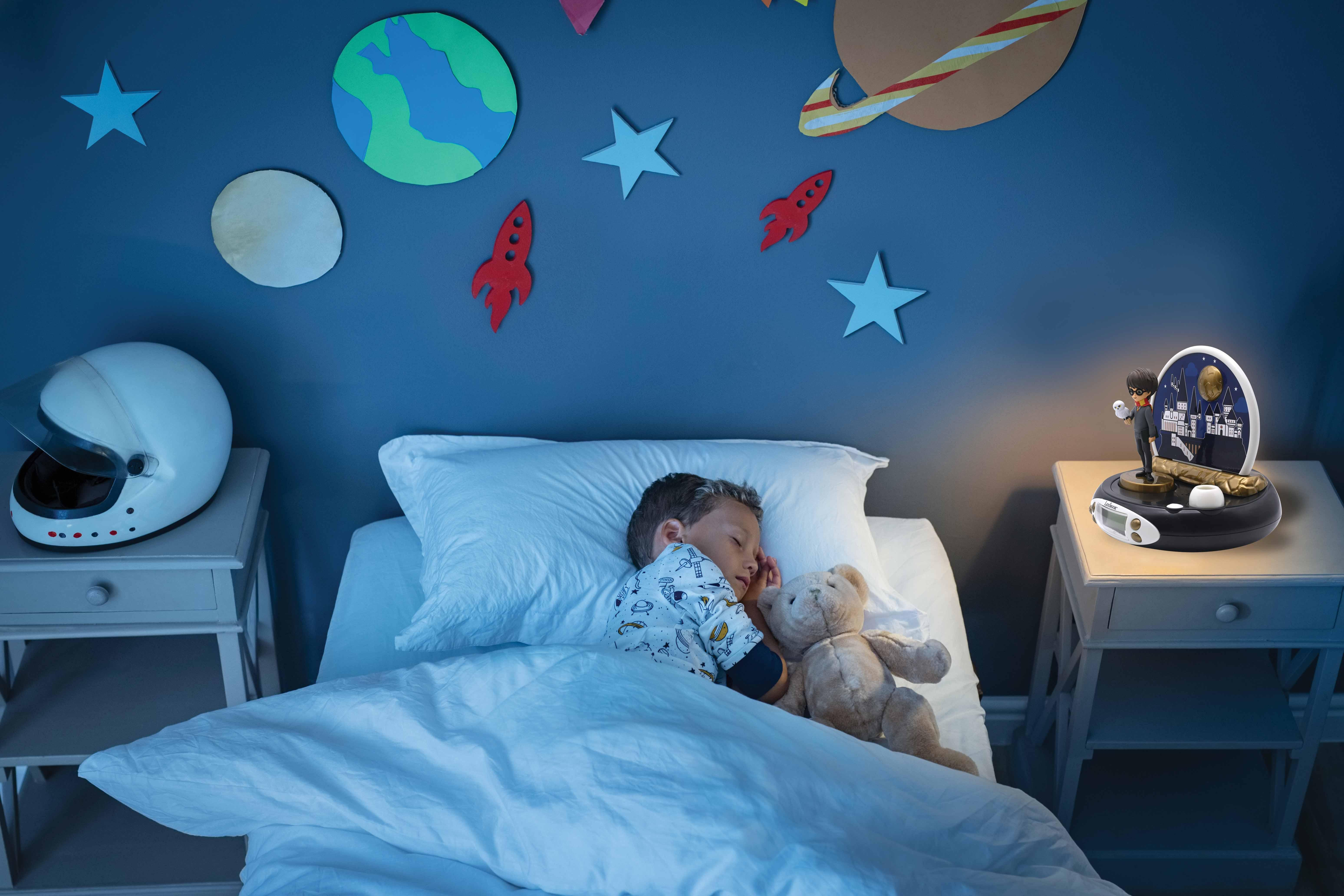 Un niño durmiendo en la cama con un oso de peluche y una luz nocturna espacial. Paredes azules con arte espacial.
