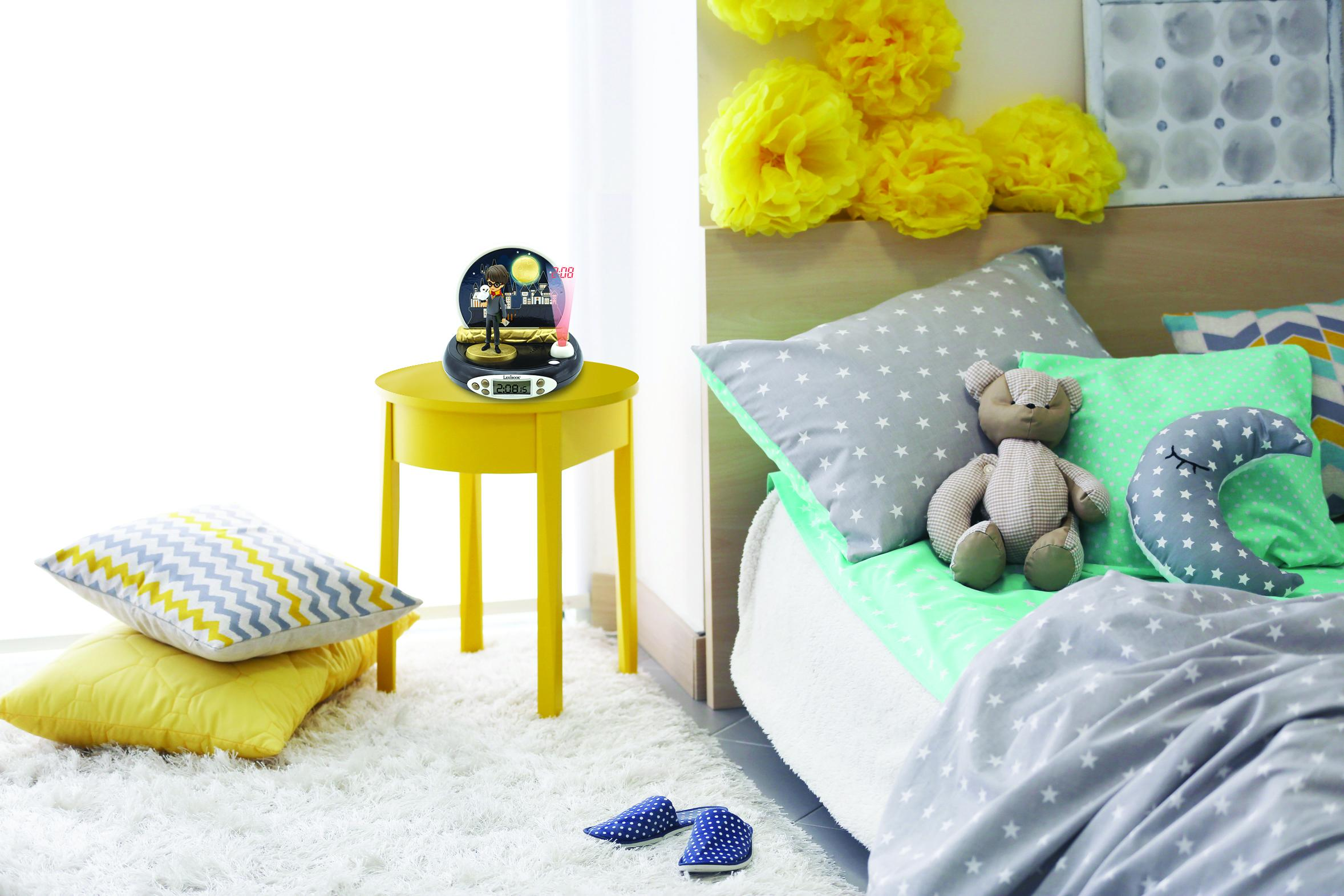 Escena de dormitorio: Mesita amarilla con reloj, cama con almohadas de estrellas y oso.