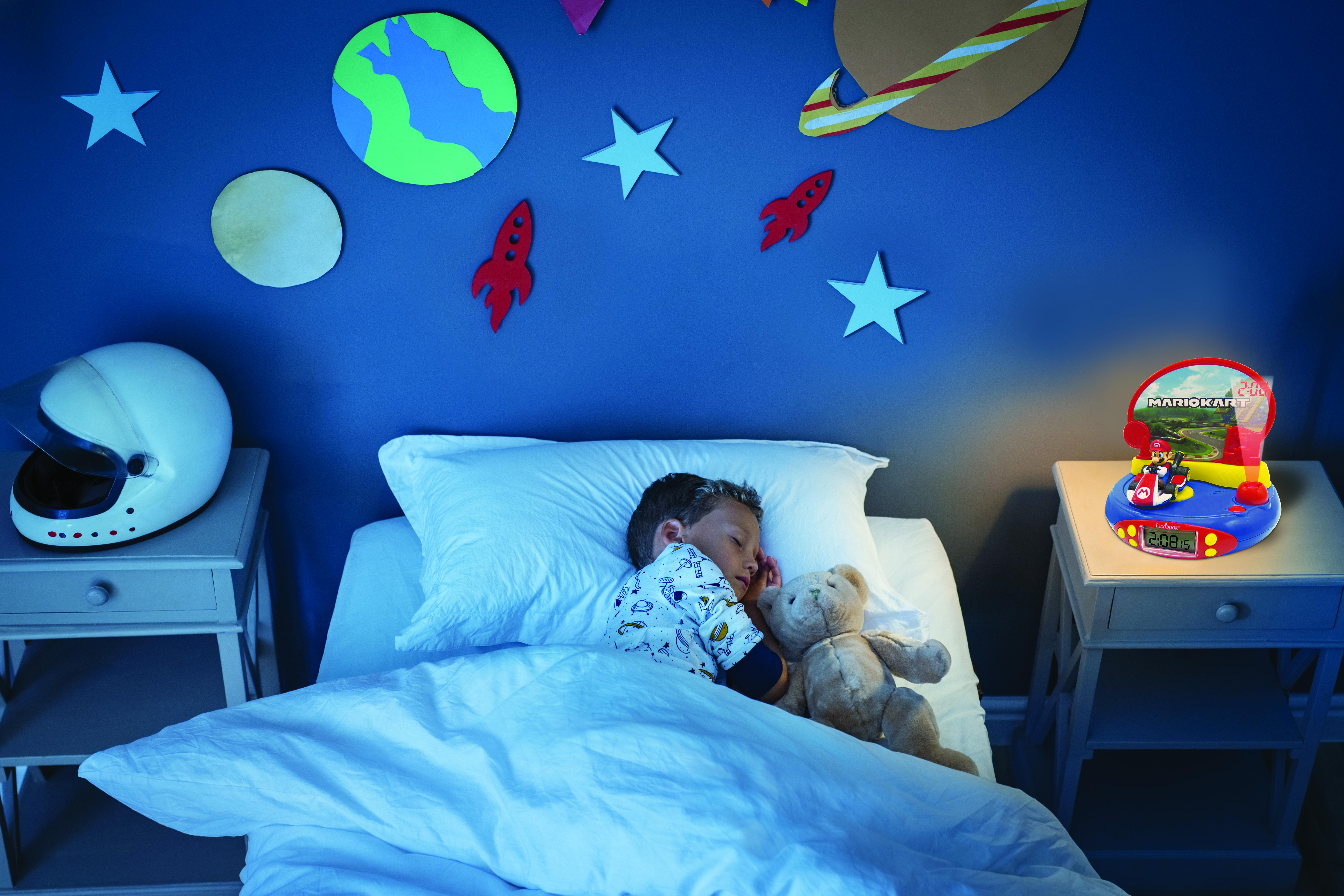 Un niño durmiendo en la cama con una luz nocturna de Mario Kart en una mesa junto a la cama.