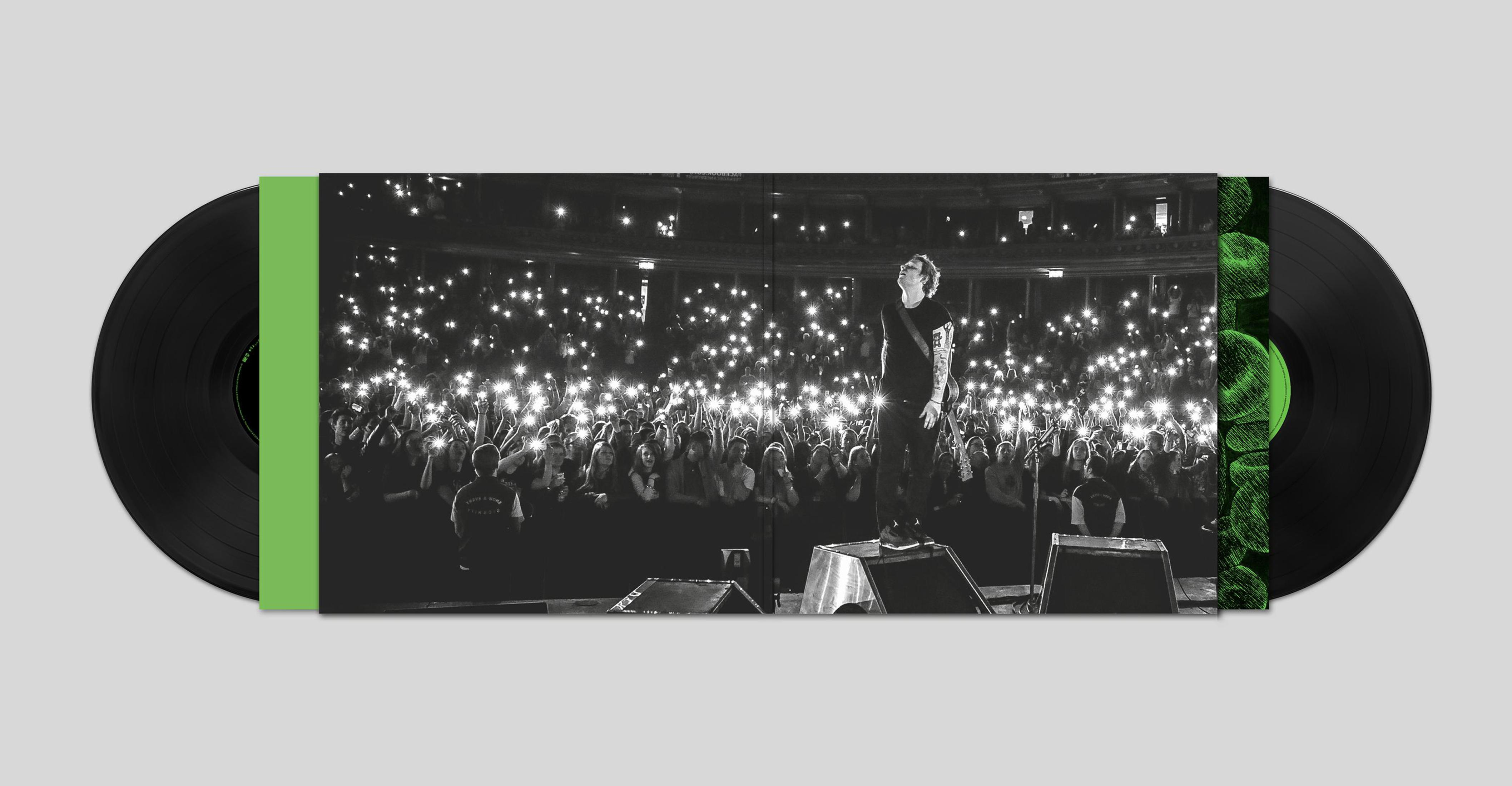 Album dal vivo con due vinili davanti. Persone con telefoni che illuminano la scena e un artista sul palco.