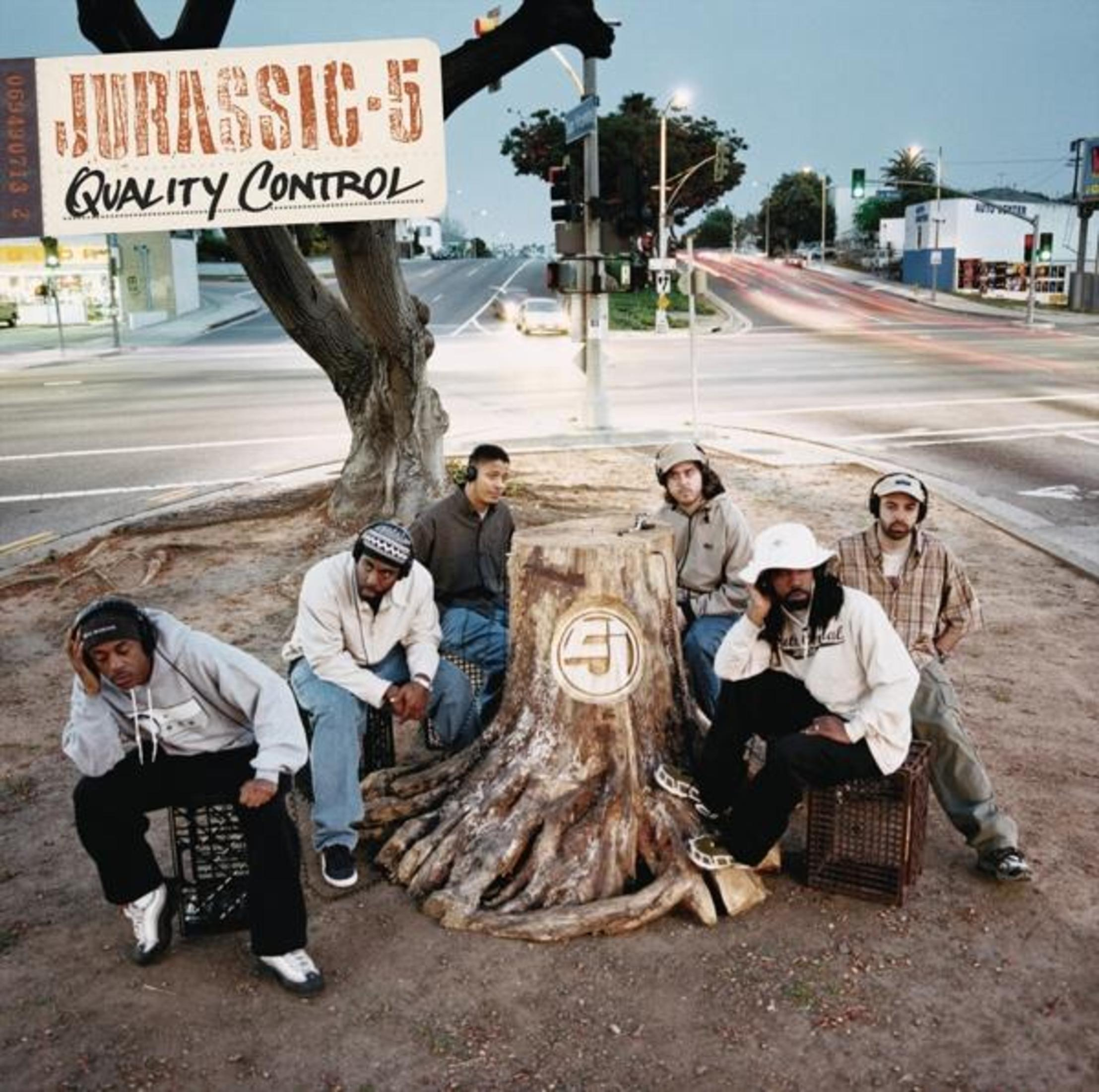 Banda Jurassic 5 su un ceppo d'albero, con sfondo di strada.