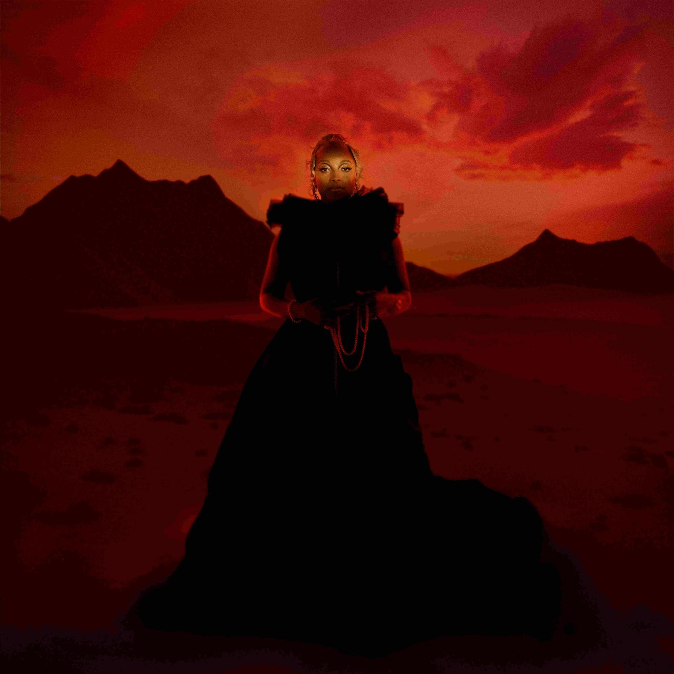 Vrouw in zwarte jurk, zonsondergang achtergrond. Rode lucht, bergen. Silhouet, kijkt naar beneden, houdt een ketting vast.