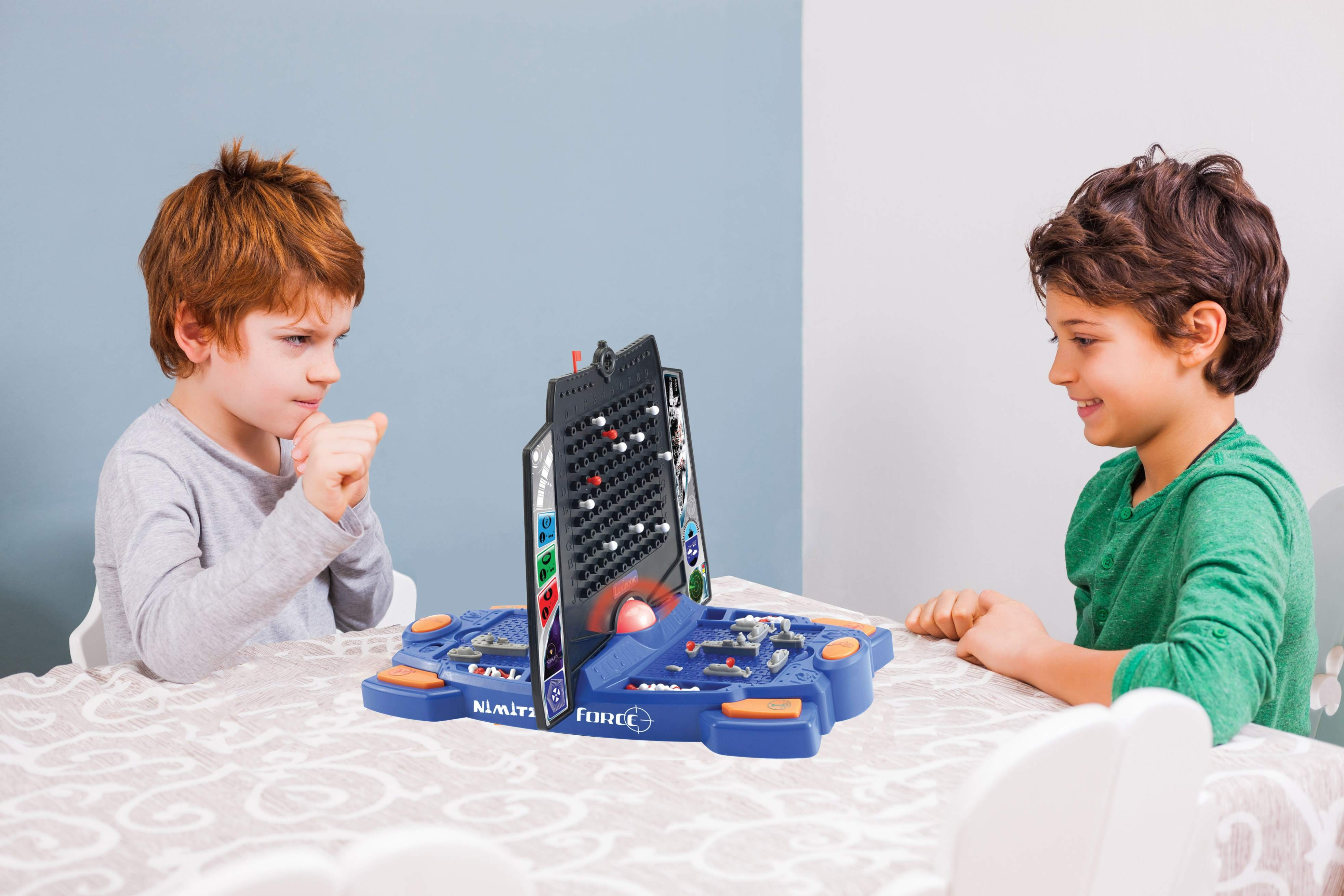 Dos niños jugando Batalla Naval. Uno serio. El otro sonríe. Mesa con juego.