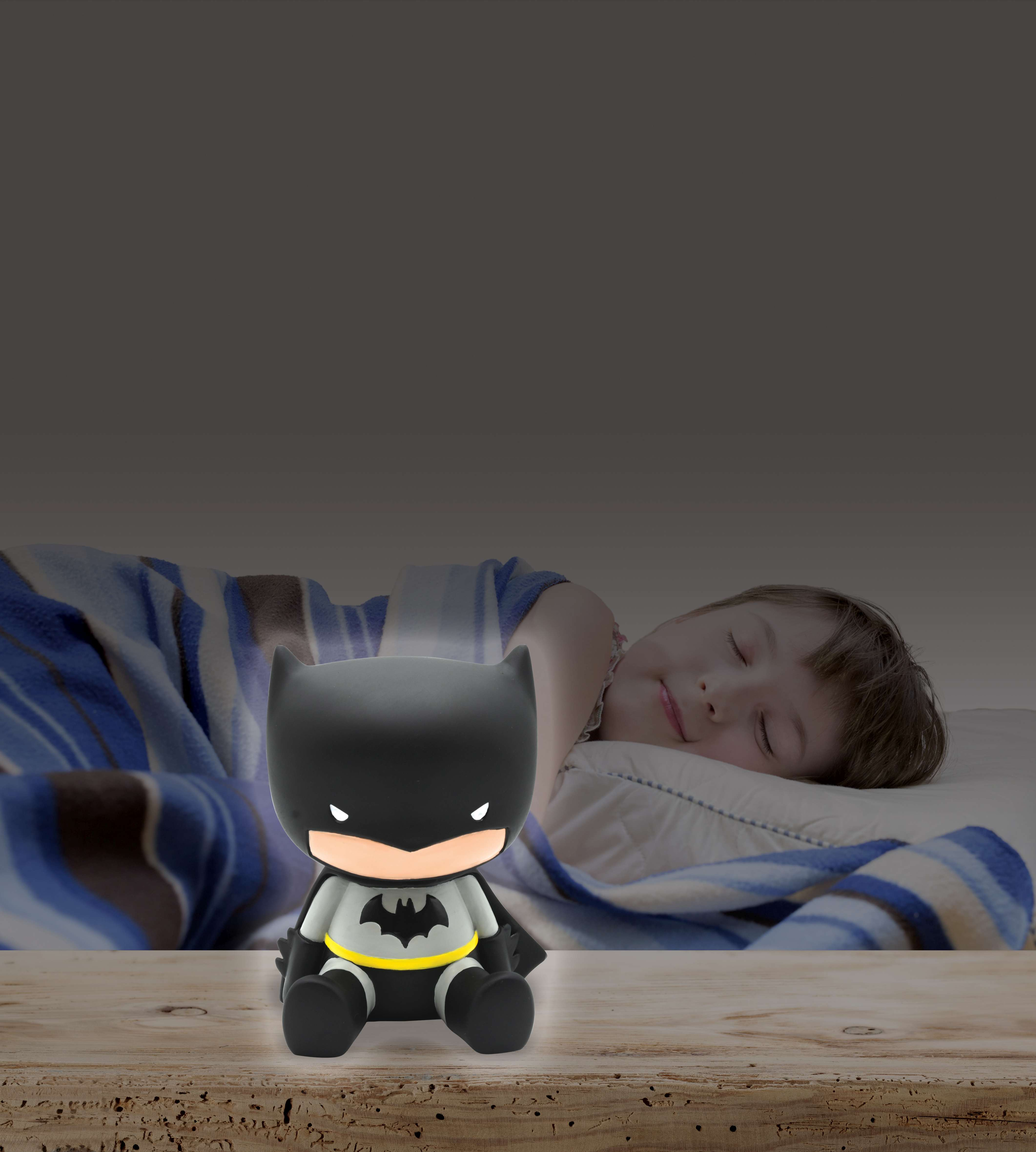 Luz nocturna de Batman sobre una mesa junto a un niño durmiendo. Está oscuro en la habitación.