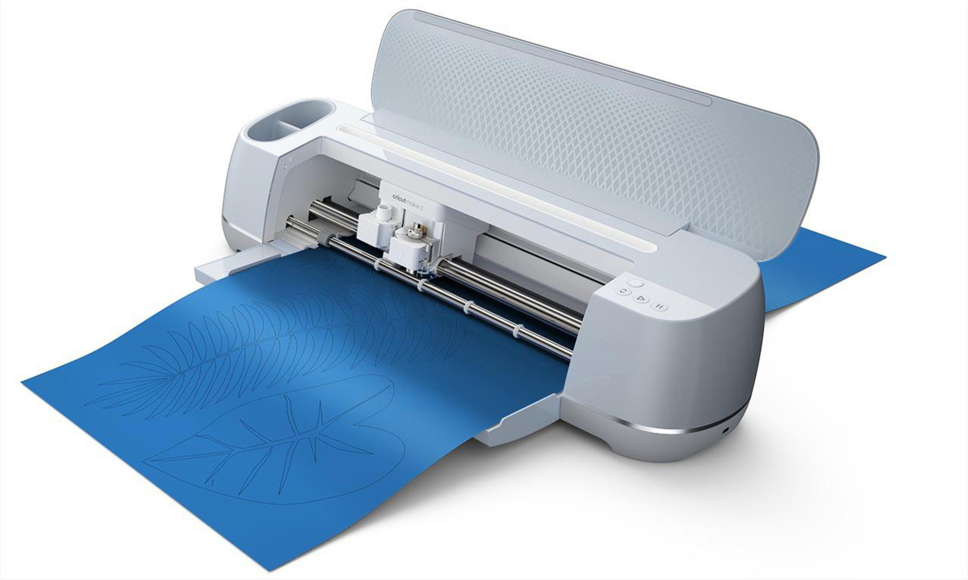 Cricut-Schneidemaschine auf blauem Blatt. Es ist weiß und grau. Das Blatt hat ein ausgeschnittenes Blattdesign.