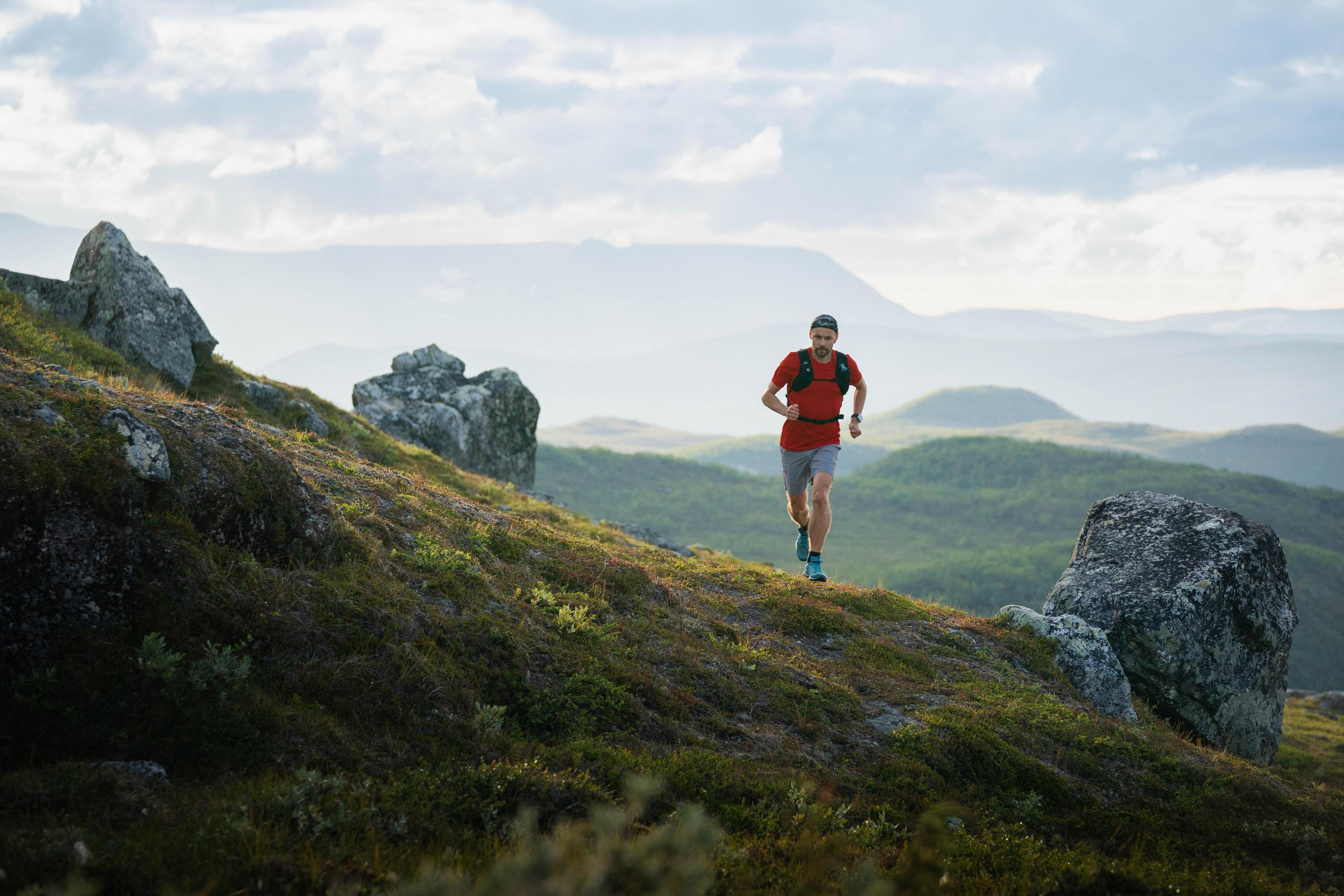 Mężczyzna biegnący pod górę na zielonym wzgórzu. Pochmurne niebo.