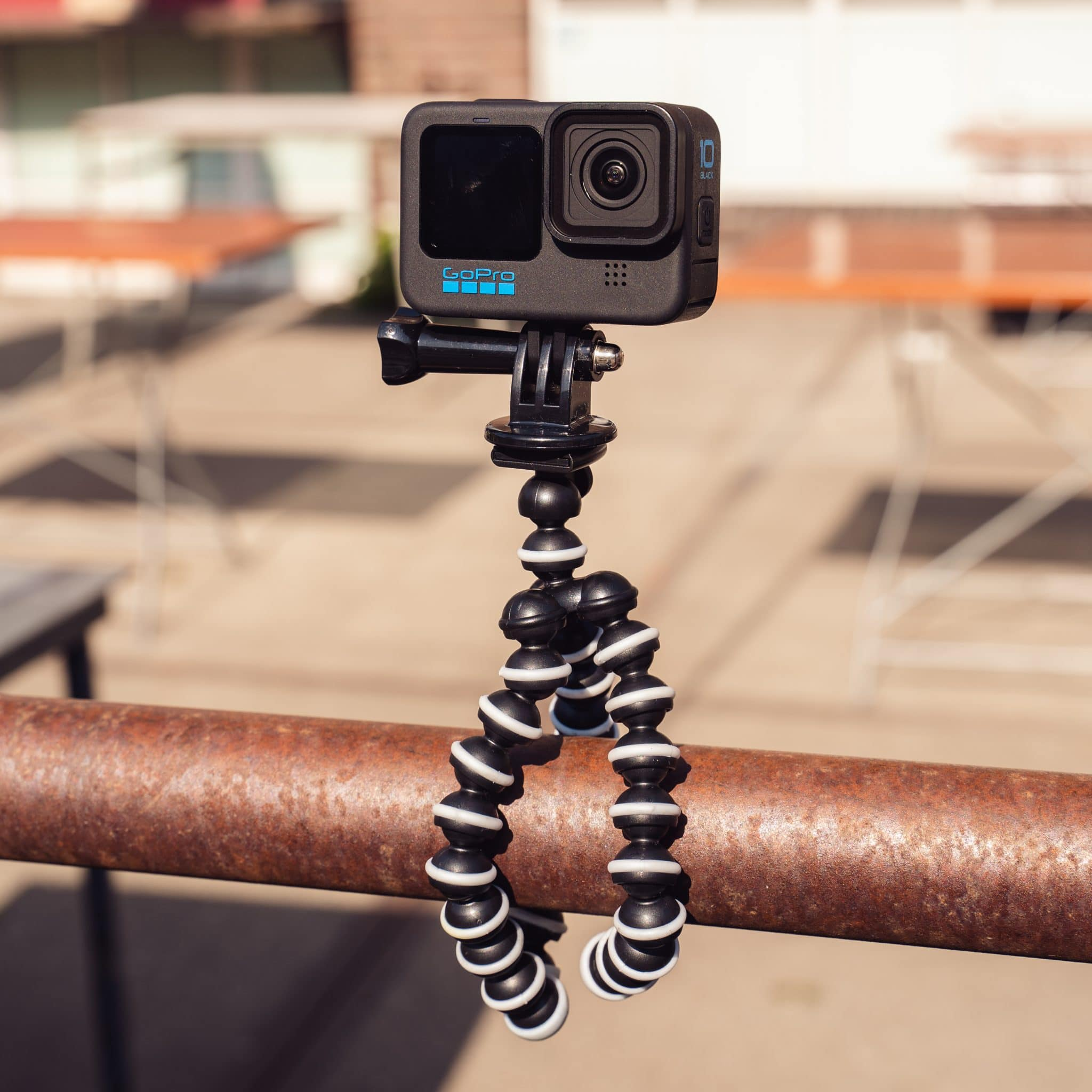 Black GoPro camera on a flexible tripod, attached to a metal bar. Background blur.