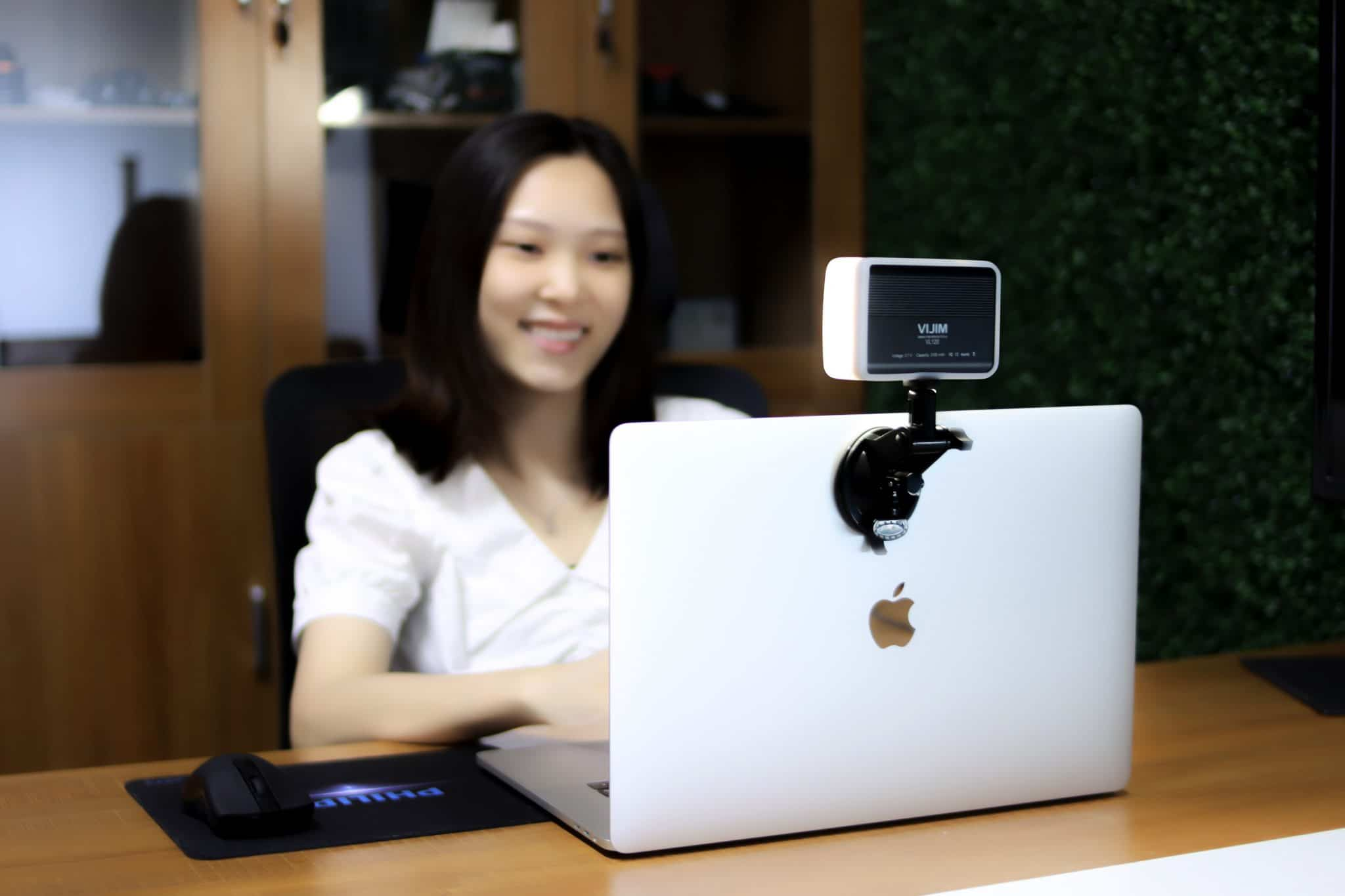 Frau lächelt bei Laptop mit Webcam-Licht, sitzt an einem Schreibtisch.