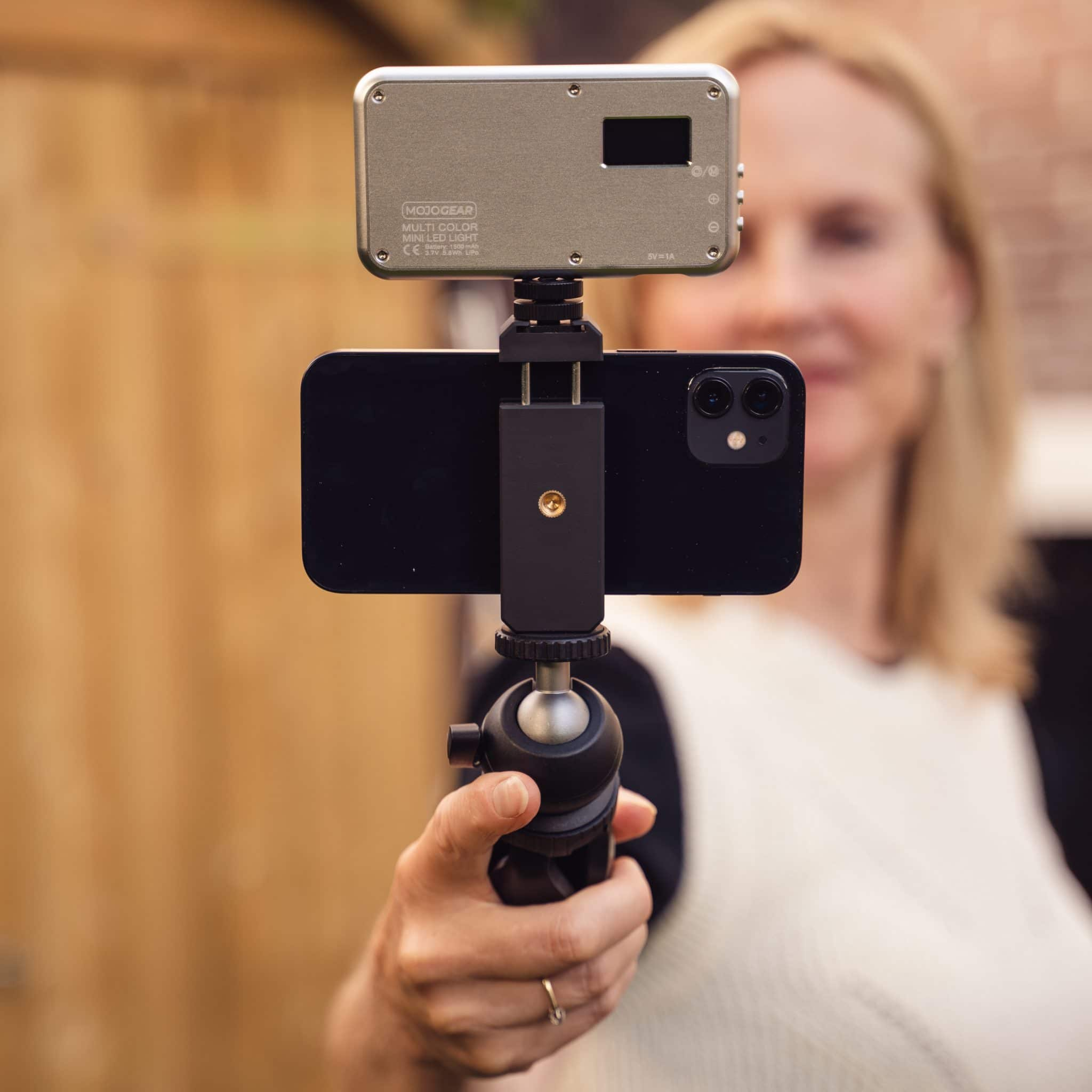 Een vrouw die een smartphone en een lamp vasthoudt voor een video. De lamp is aan de telefoon bevestigd.