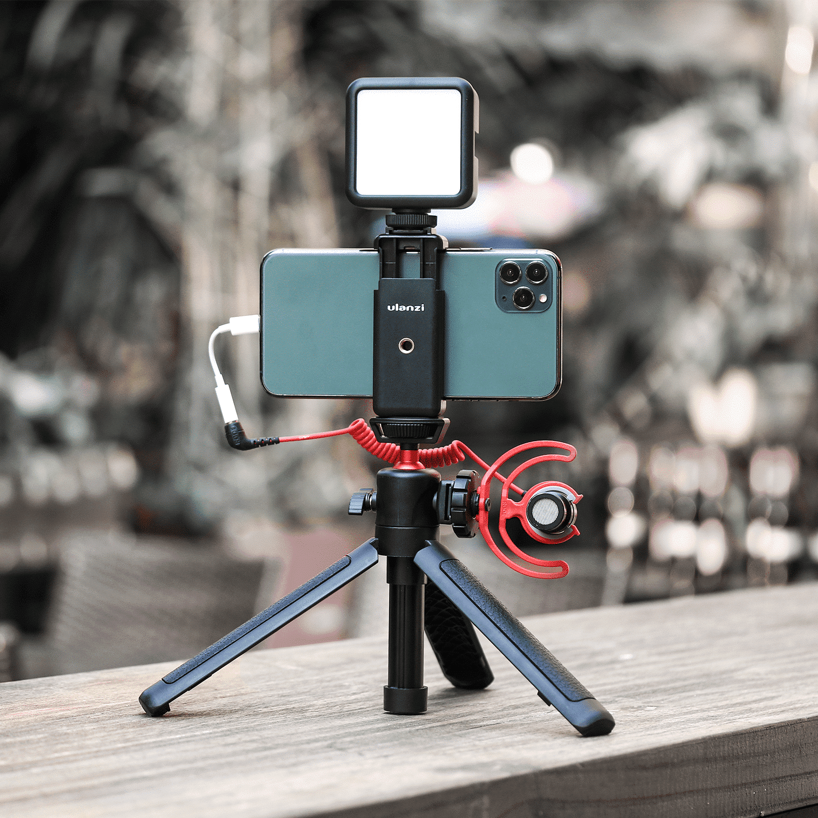 Un téléphone avec une lumière et un microphone sur un trépied. Fond extérieur flou.