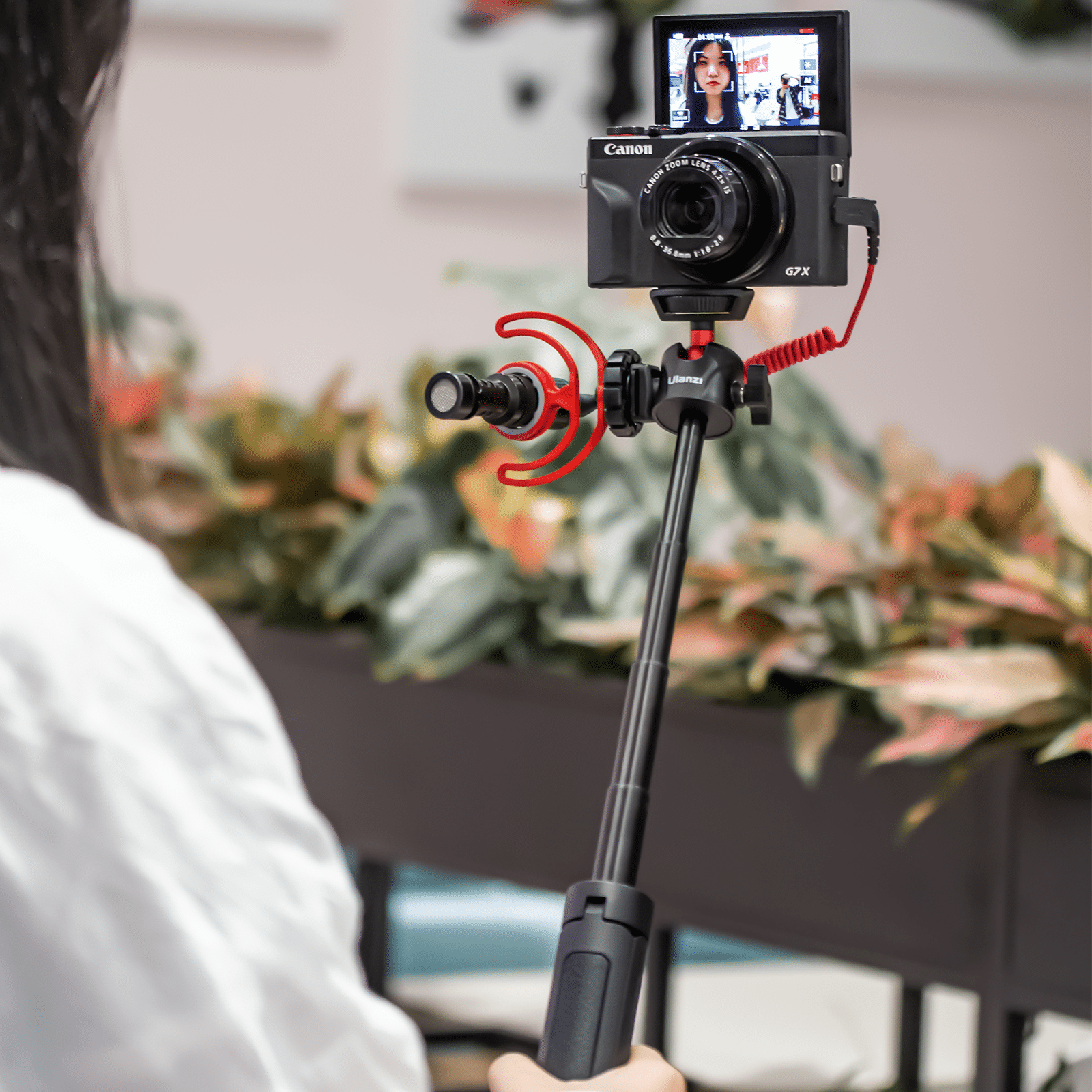 Personne filmant avec une caméra Canon attachée à un microphone et une perche à selfie.