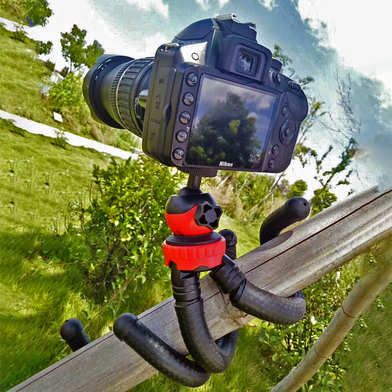 Appareil photo Nikon noir sur un trépied flexible fixé sur un rail en bois. Fond vert.