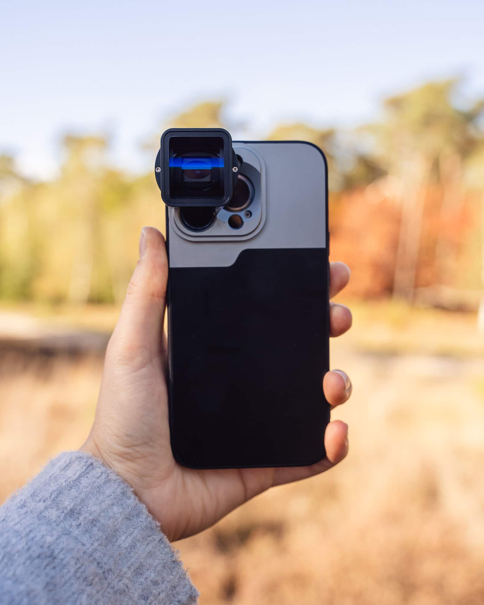 A person holding a smartphone with a lens attachment, focus is on the lens.