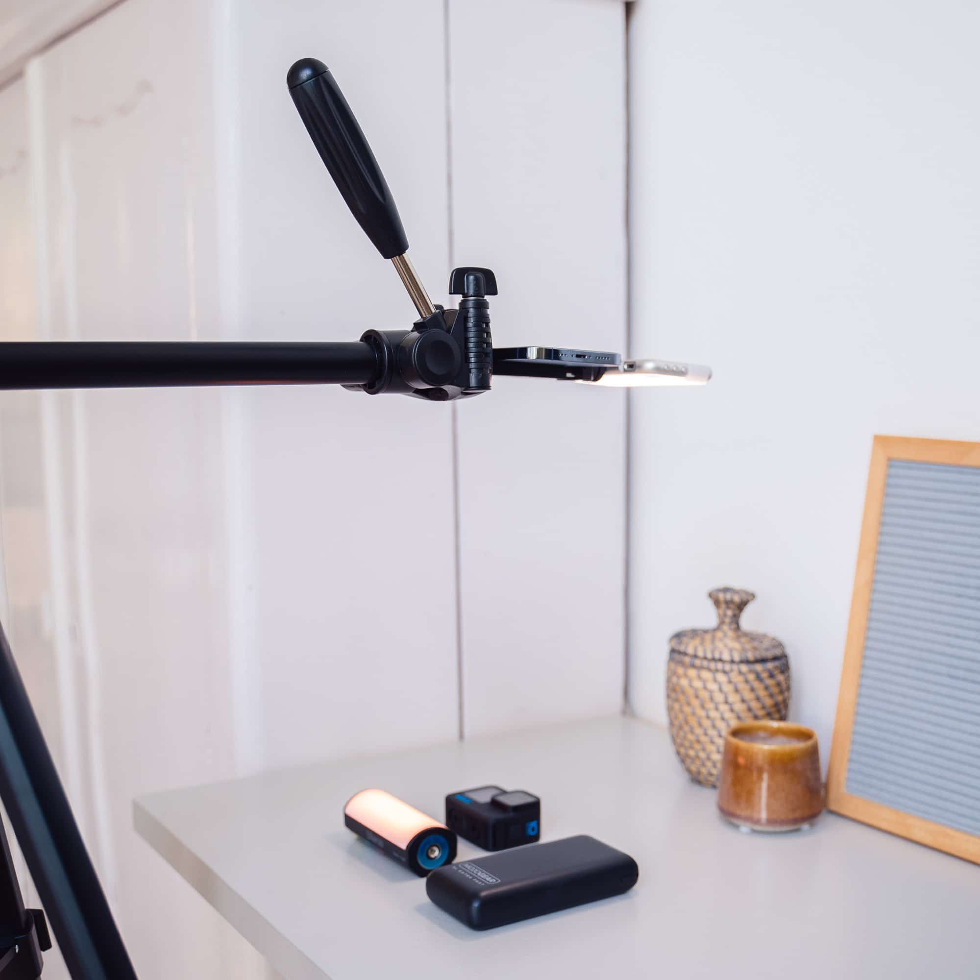 Tripod holding phone, with accessories like charger and camera.