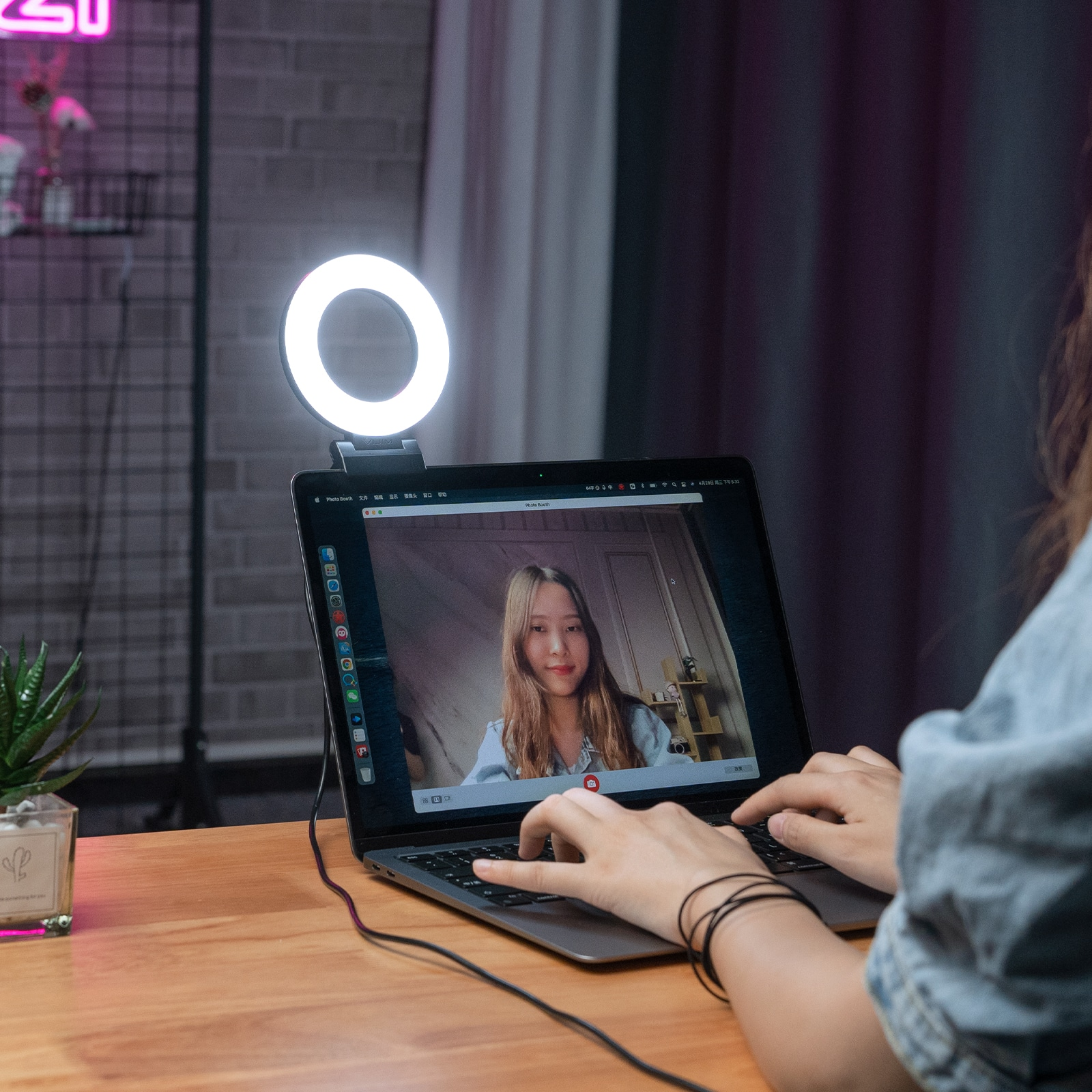 A woman on a laptop, illuminated by a ring light. The screen shows a video call.
