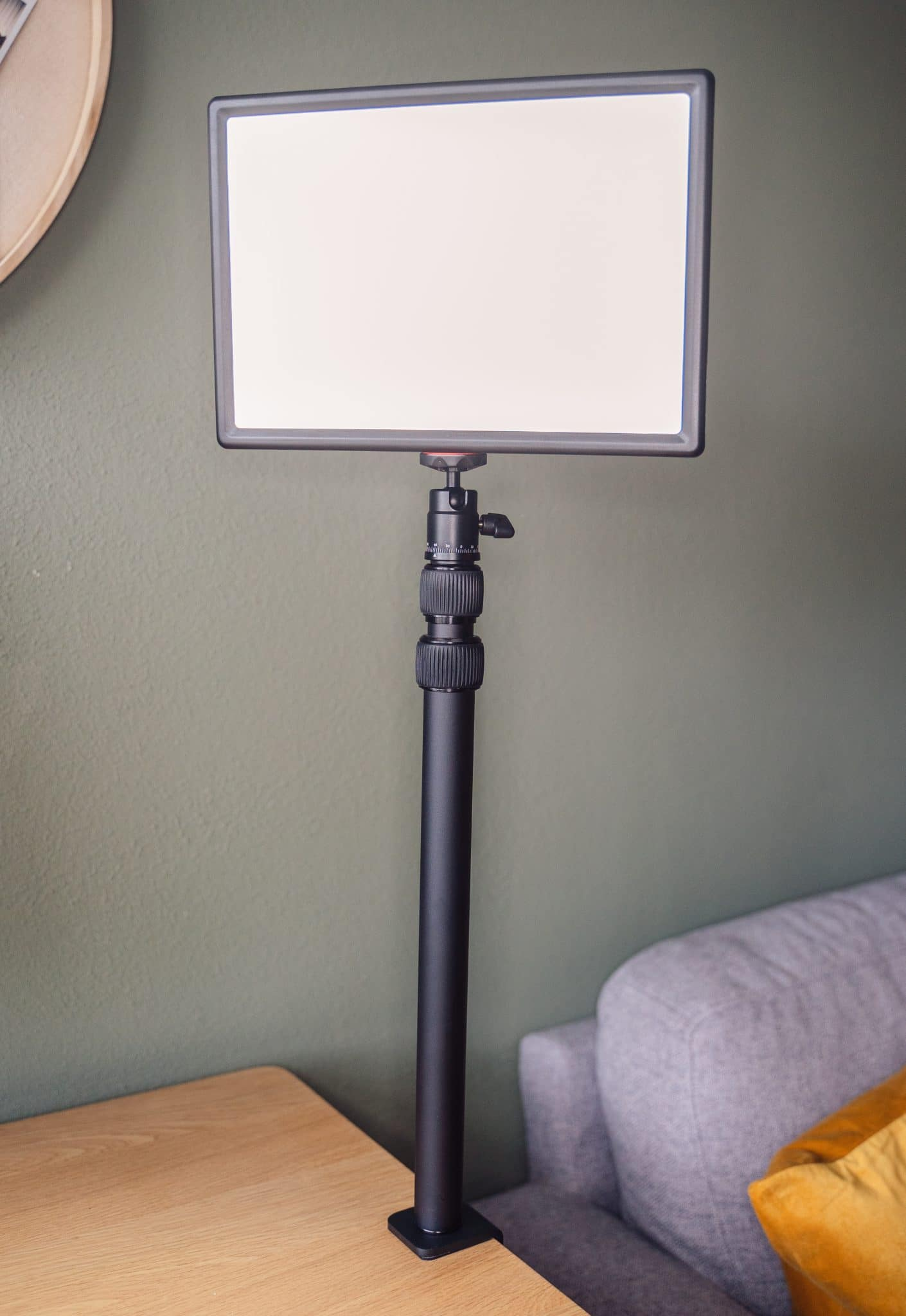 Een rechthoekige LED-lamp is gemonteerd op een zwart statief. Het statief staat op een houten tafel.