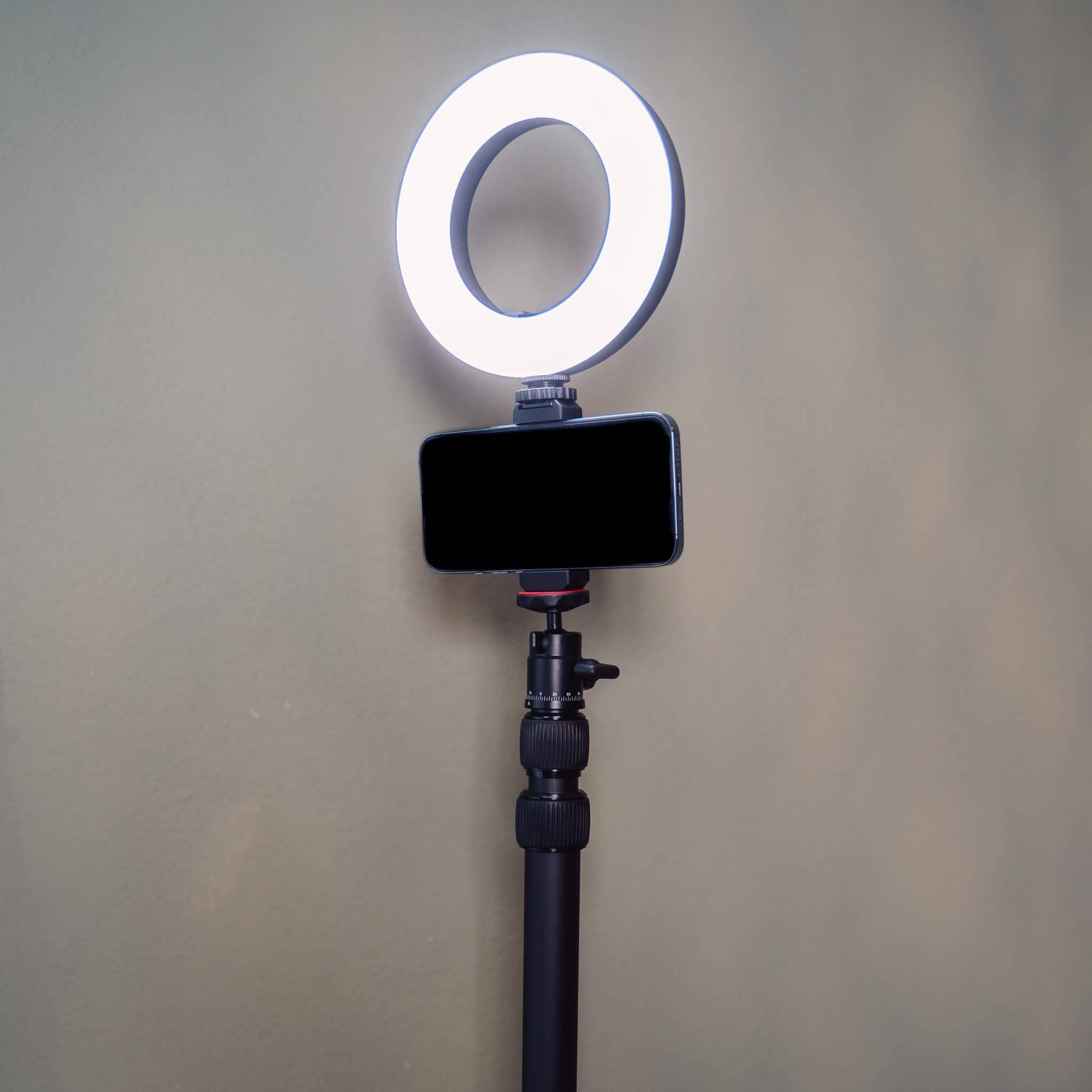 Een telefoon is op een statief gemonteerd met een ringlicht. Het licht is aan en de telefoon is zwart.