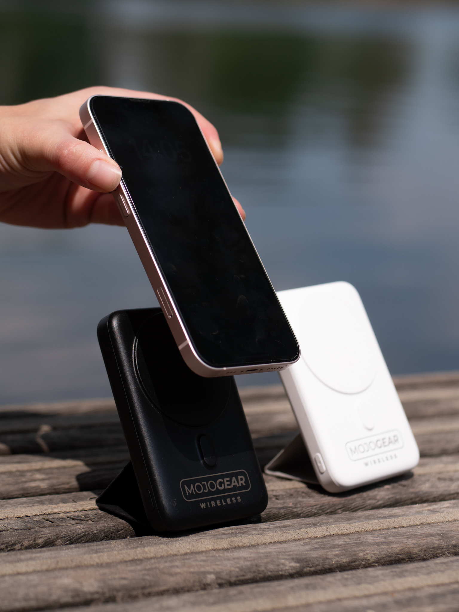 Een persoon die een telefoon boven twee draadloze opladers houdt. Eén oplader is zwart, de andere wit, op een houten oppervlak.