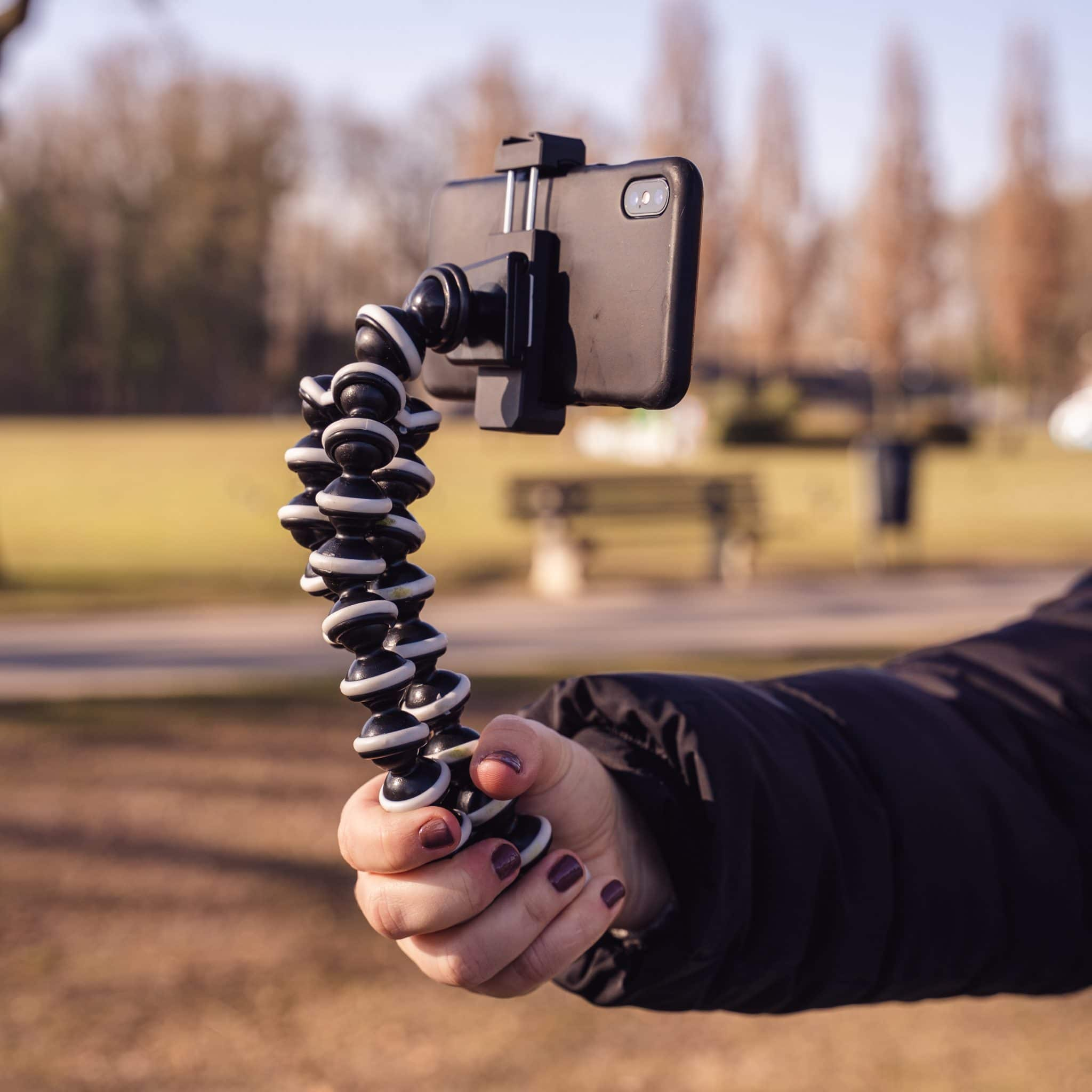 A person's hand holding a flexible phone mount. The phone is black, and the mount is black and white.