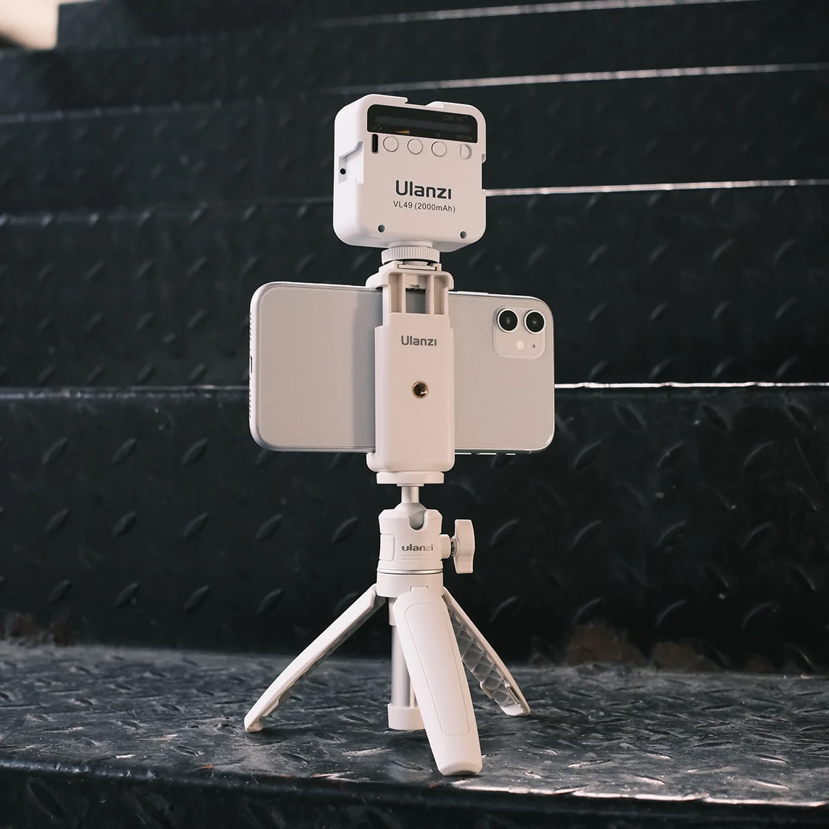 Biały telefon z lampą Ulanzi i statywem na metalowych schodach.