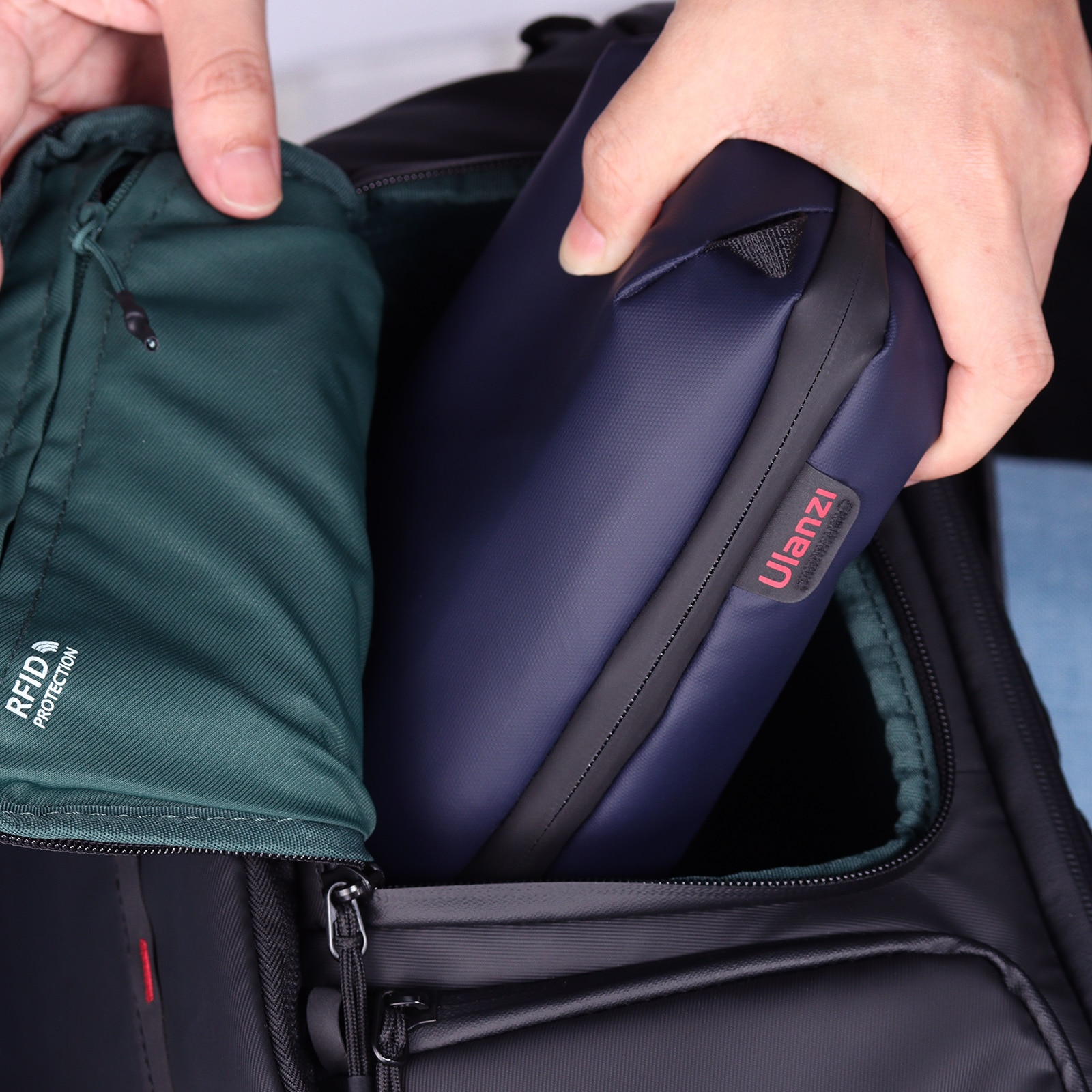 Mains plaçant un sac bleu dans un sac à dos noir. Intérieur vert. Logo Ulanzi visible.