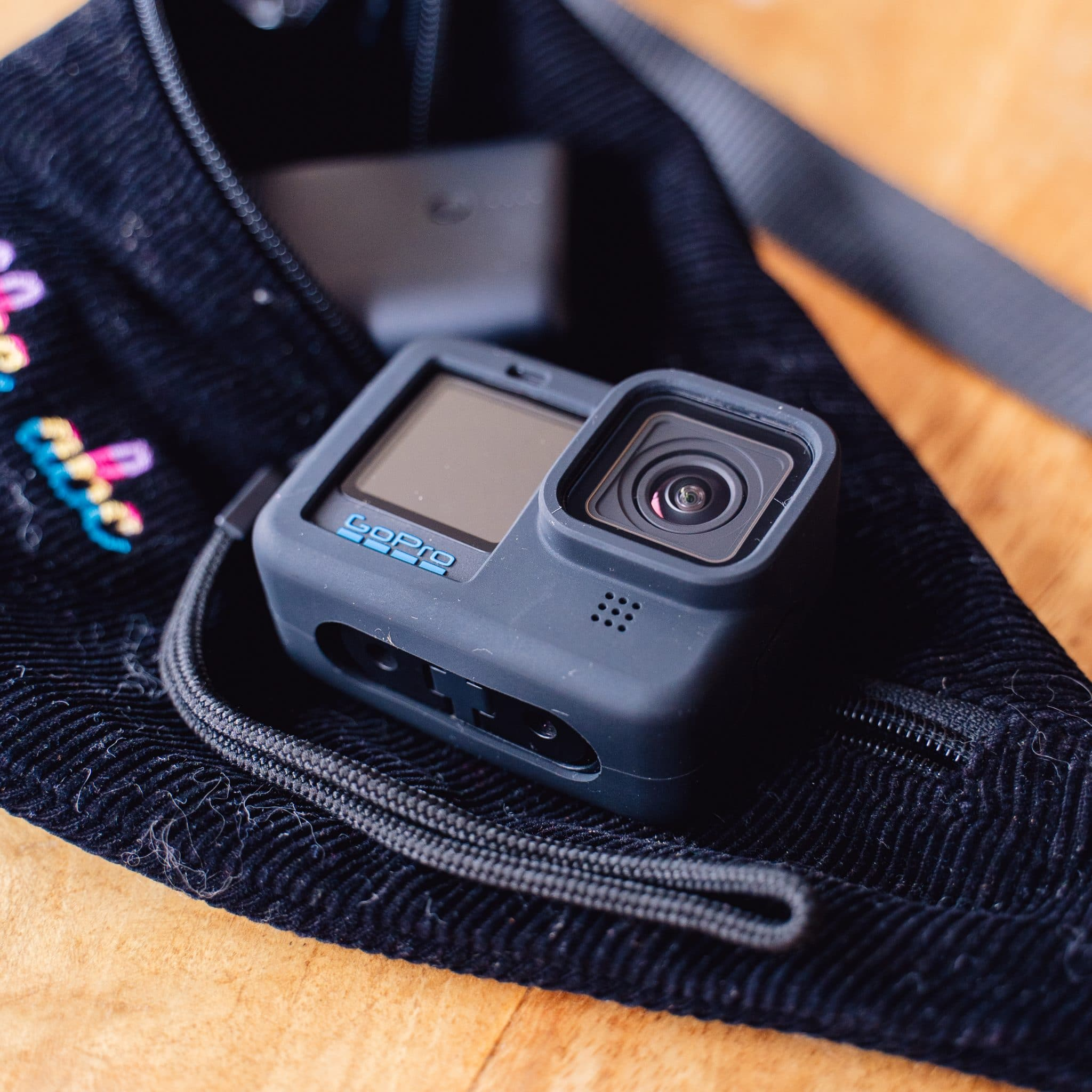 GoPro-camera in een zwarte hoes in een zwart zakje, op een houten oppervlak.