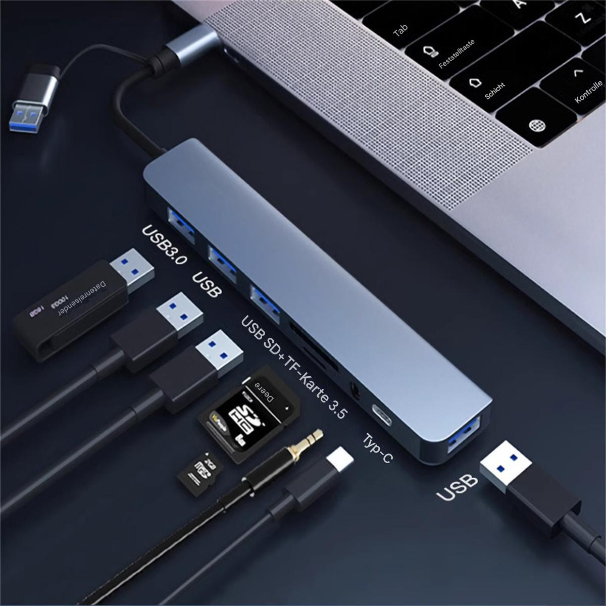 Ein Hub mit USB-Anschlüssen und angeschlossenen Geräten. Ein Laptop ist im Hintergrund.