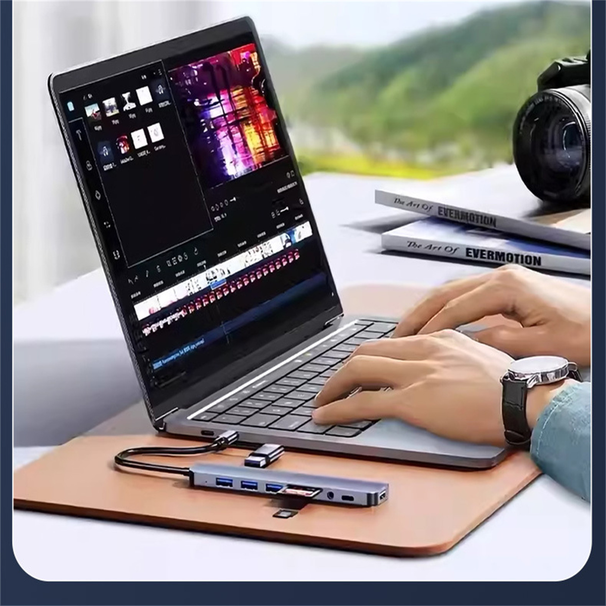 Person arbeitet an Laptop mit Hub. Bücher und Kamera im Hintergrund.