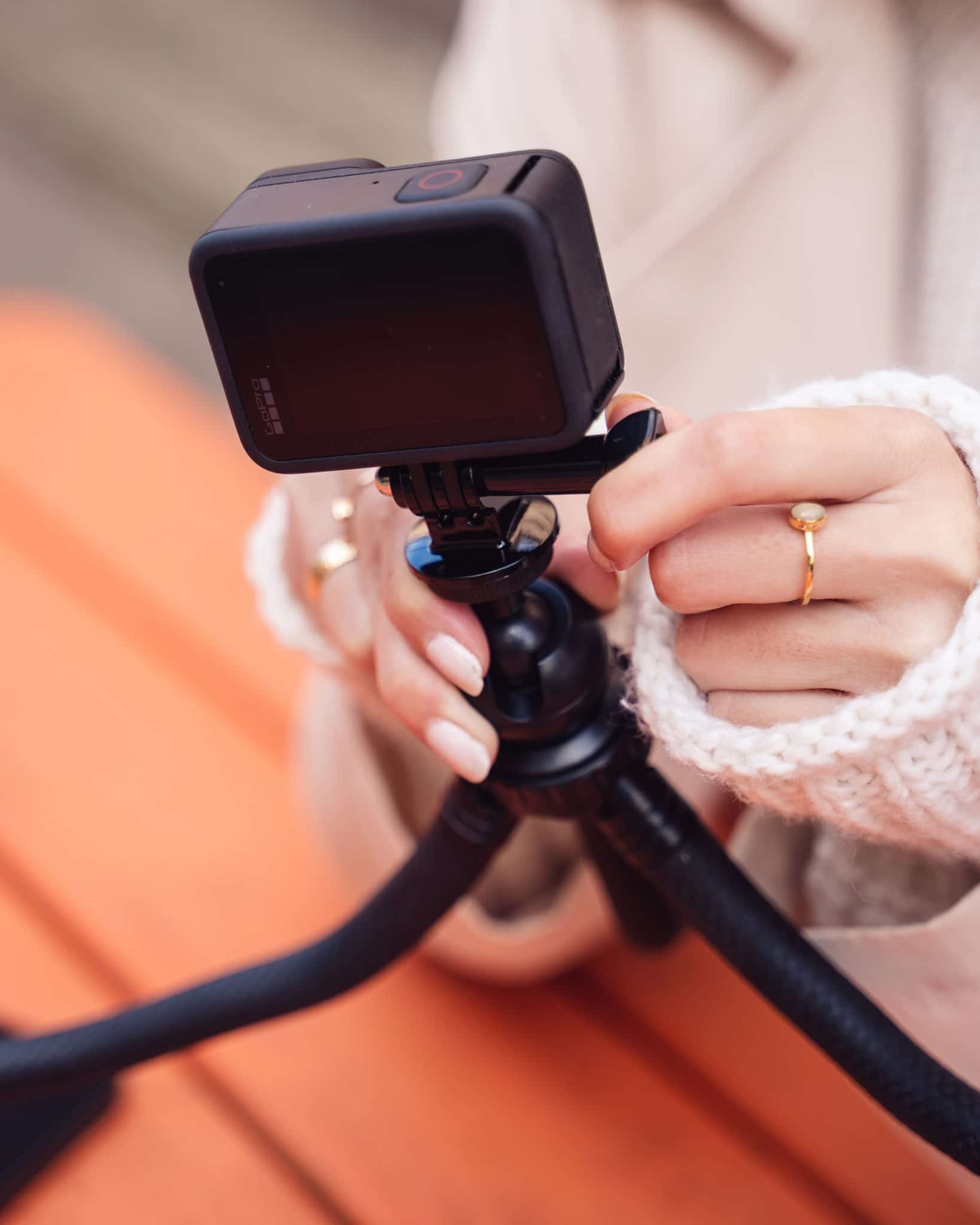 Hände einer Frau halten eine schwarze GoPro-Kamera an einem Mini-Stativ, im Freien.