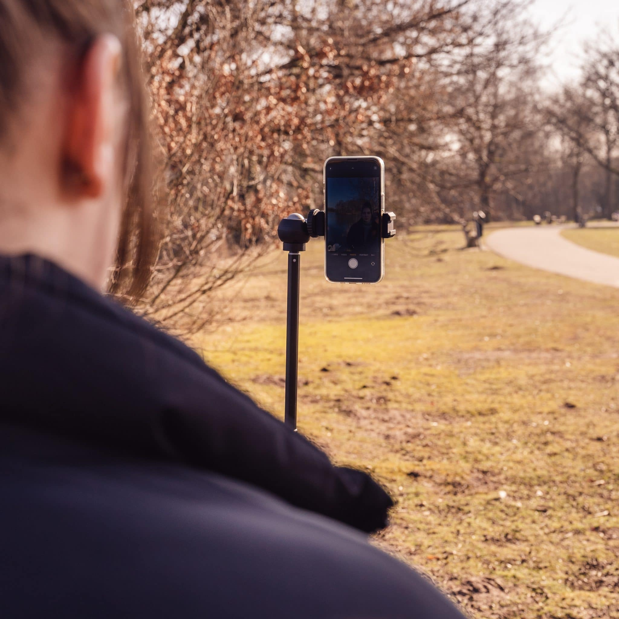 Person filming with phone on a selfie stick in a park.