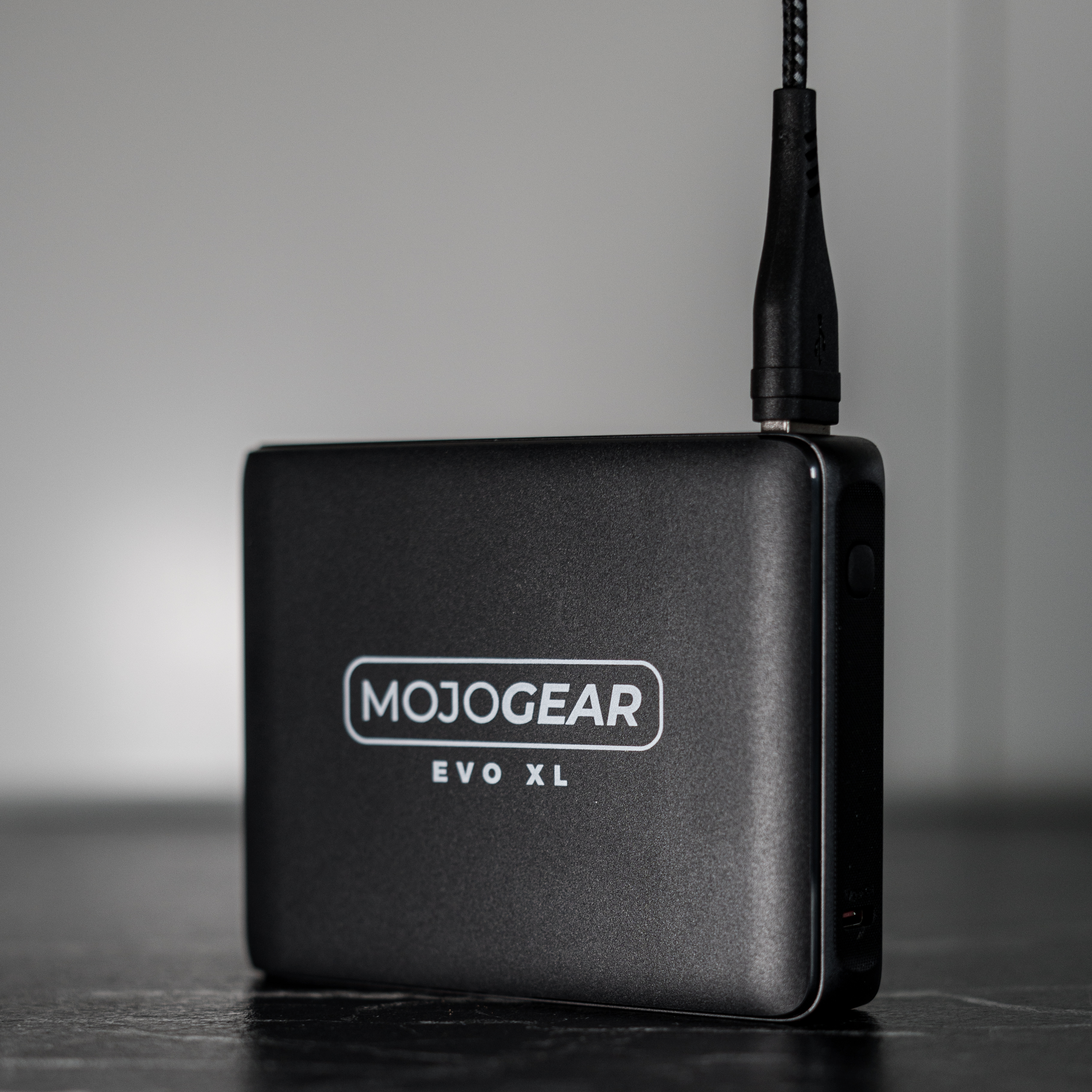 Un appareil carré noir avec un câble noir branché. L'appareil porte le mot MOJOGEAR.