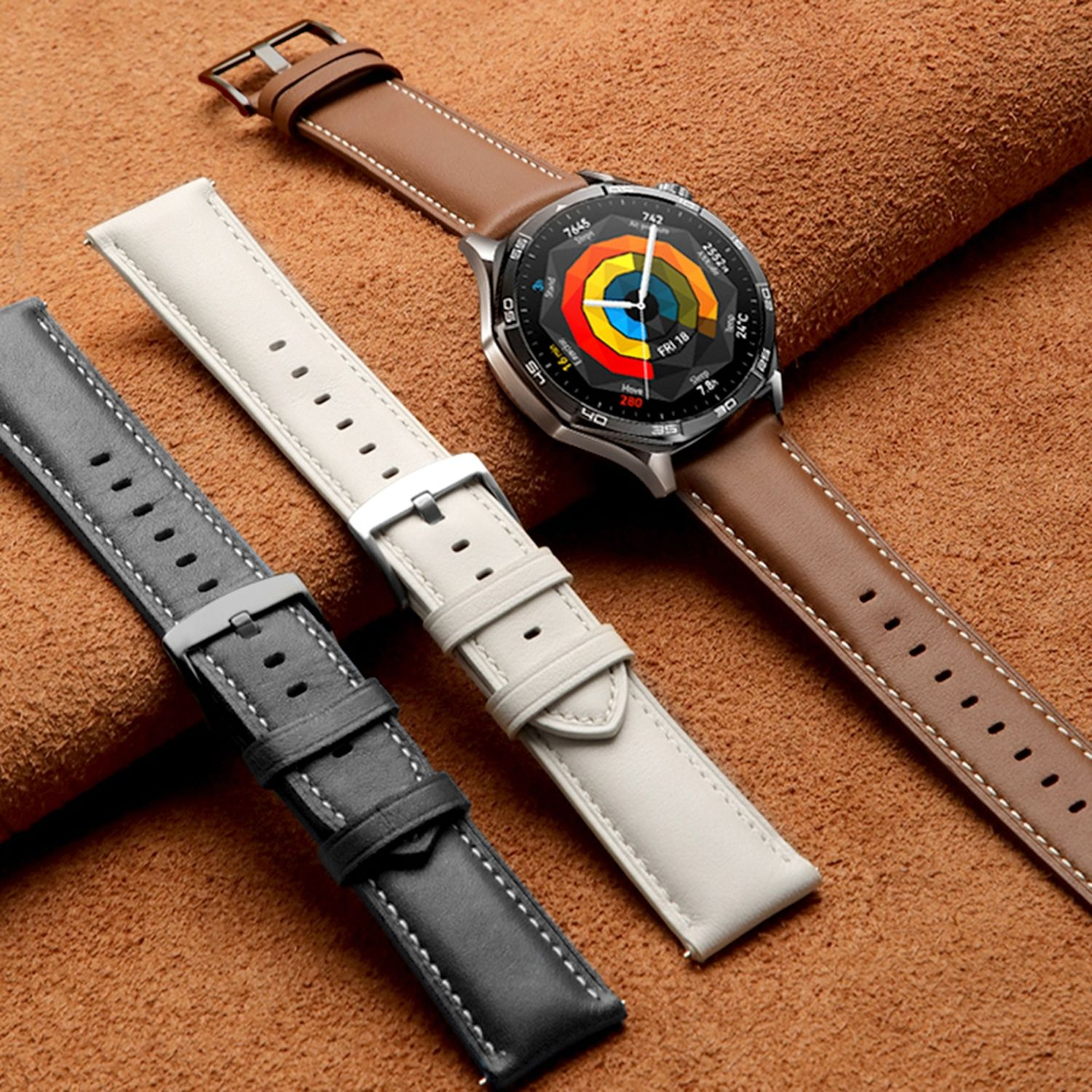 Smartwatch mit braunem Lederarmband, mit zwei weiteren Armbändern, cremefarben und grau, auf einer braunen Lederoberfläche.