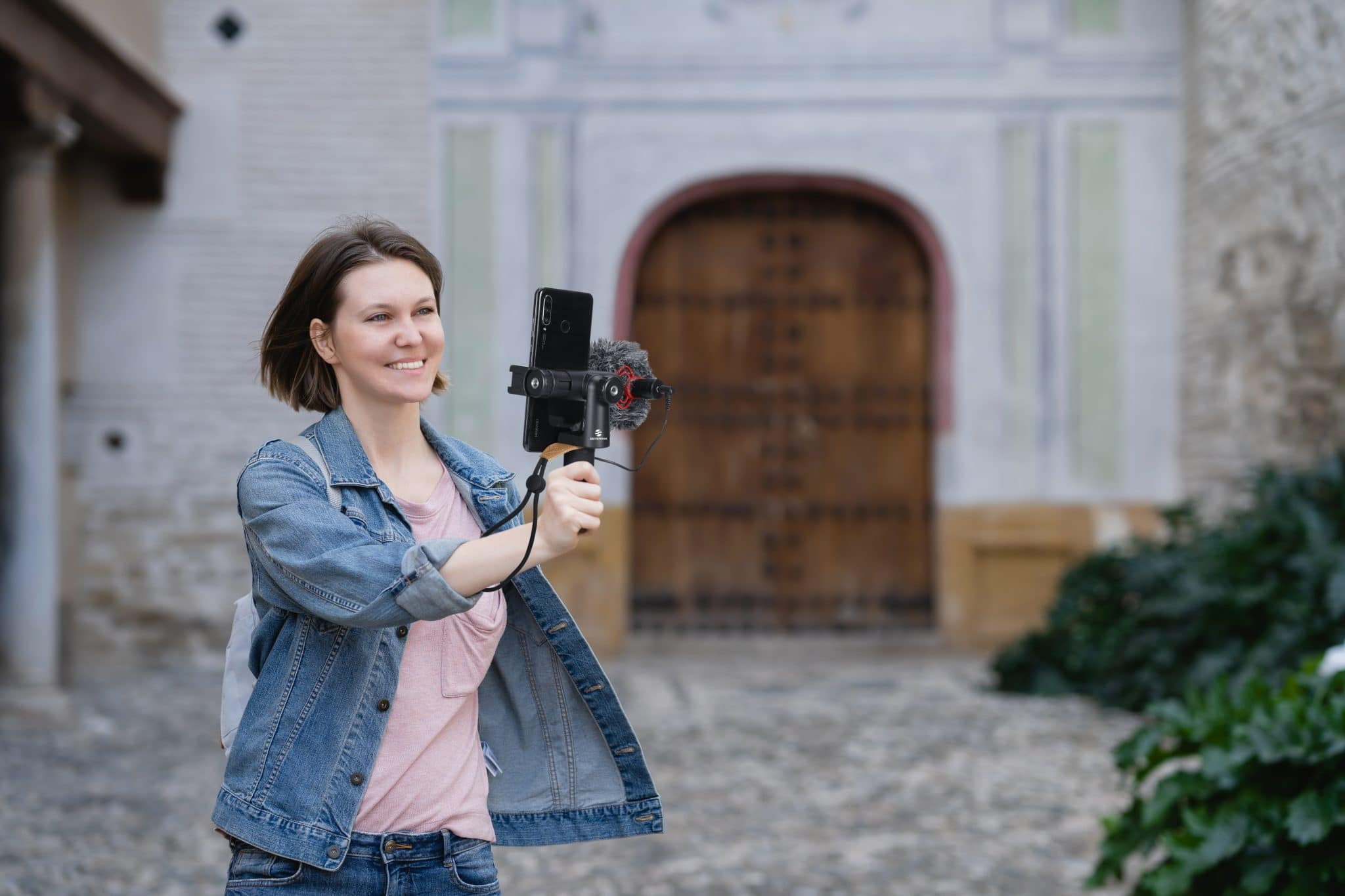 Kobieta vloguje za pomocą smartfona i mikrofonu przed budynkiem.