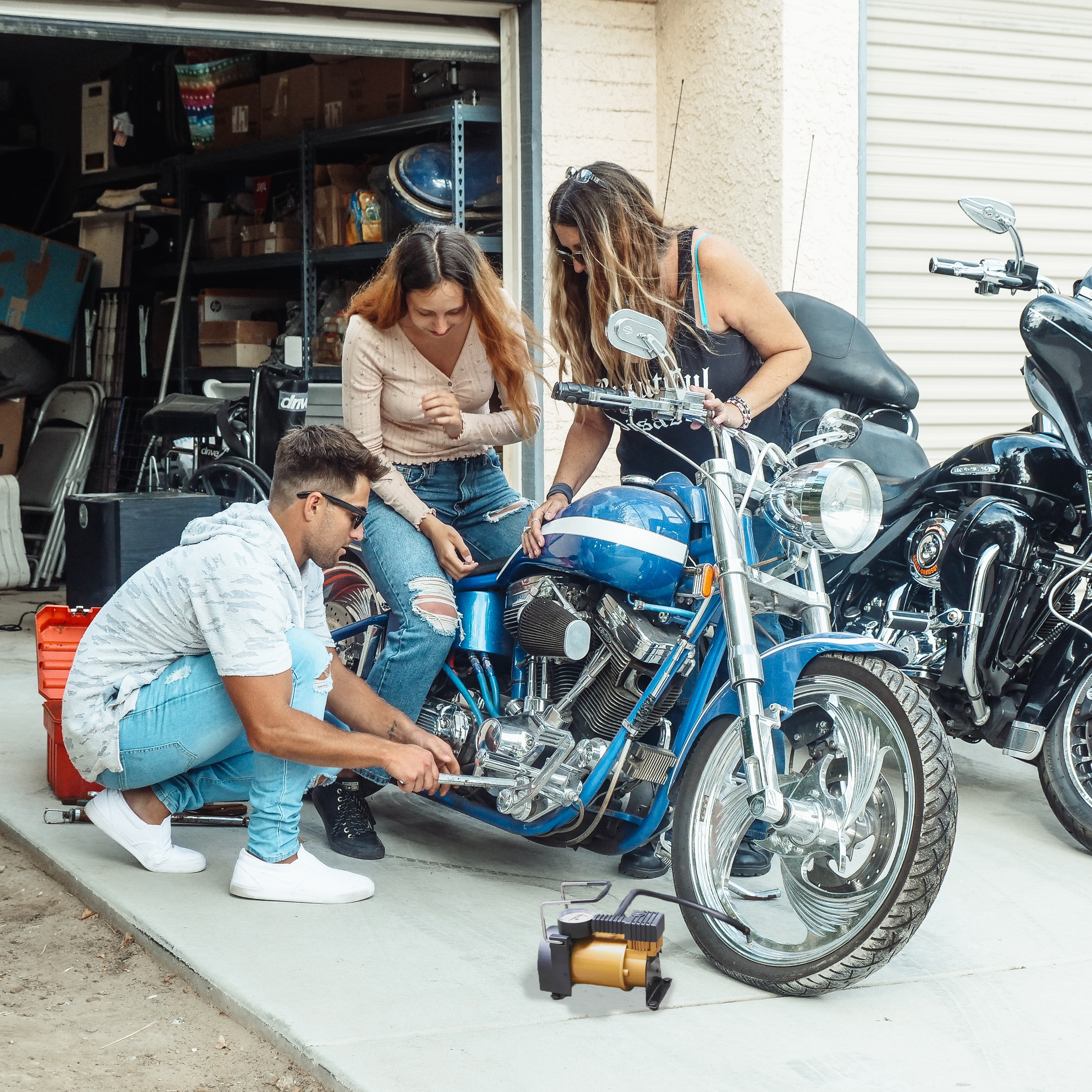 Tre persone che lavorano su una moto blu. Un'ambientazione da garage con attrezzi e deposito.