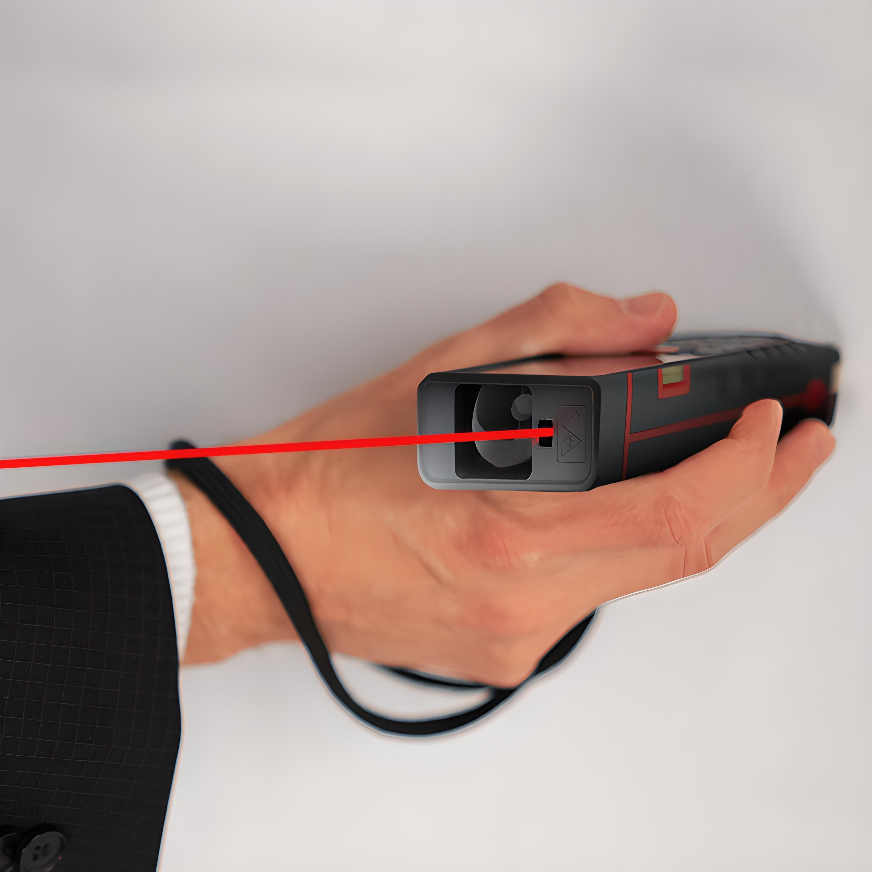Hand, die ein schwarzes Laser-Entfernungsmessgerät hält, roter Strahl, der auf eine weiße Oberfläche projiziert wird.