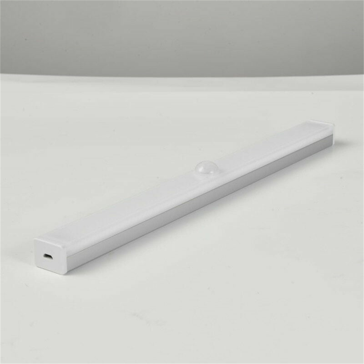 Ein weiß-grauer LED-Lichtbalken mit Sensor auf einer weißen Oberfläche.