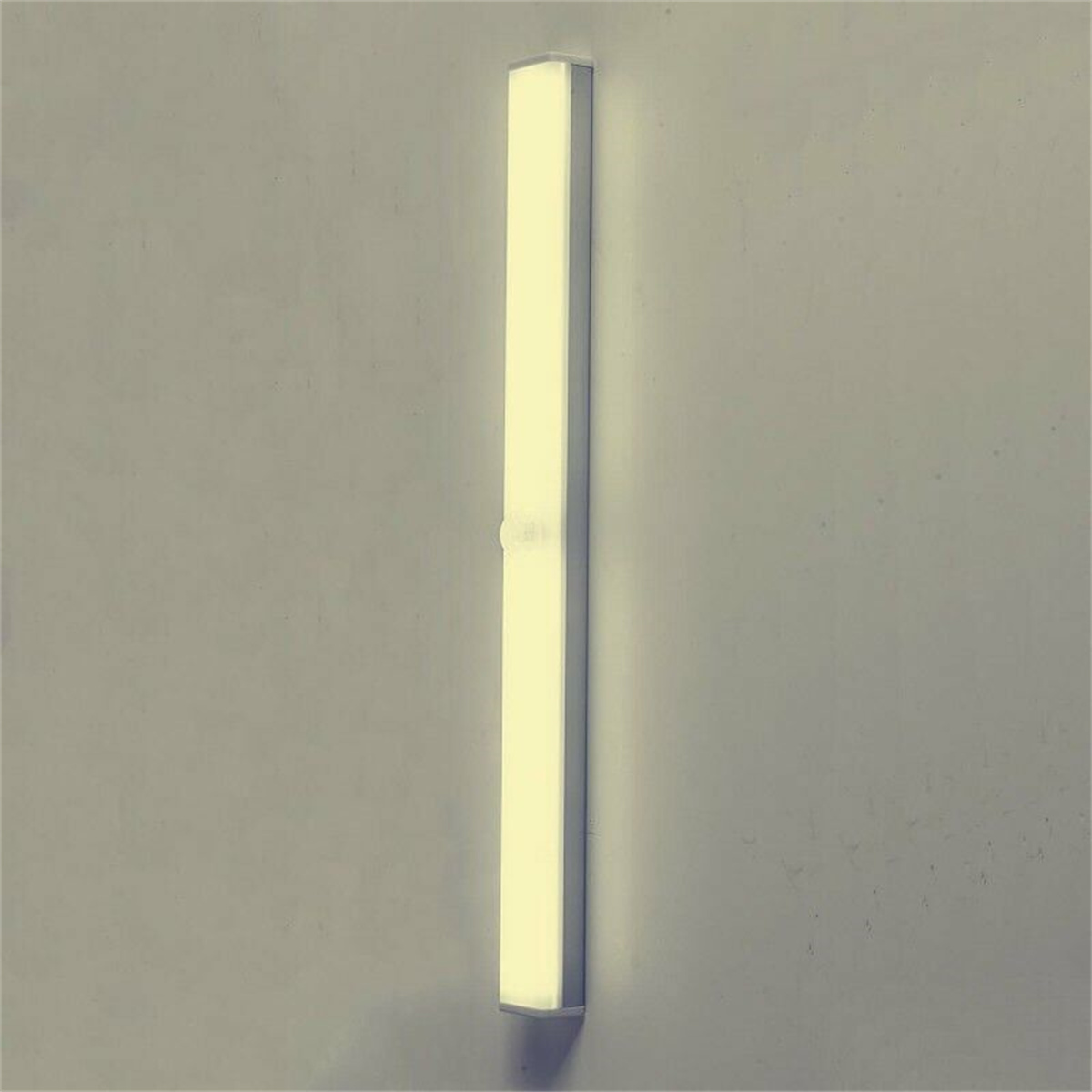 Eine lange, rechteckige LED-Leuchte, die an einer hellgrauen Wand montiert ist, eingeschaltet.