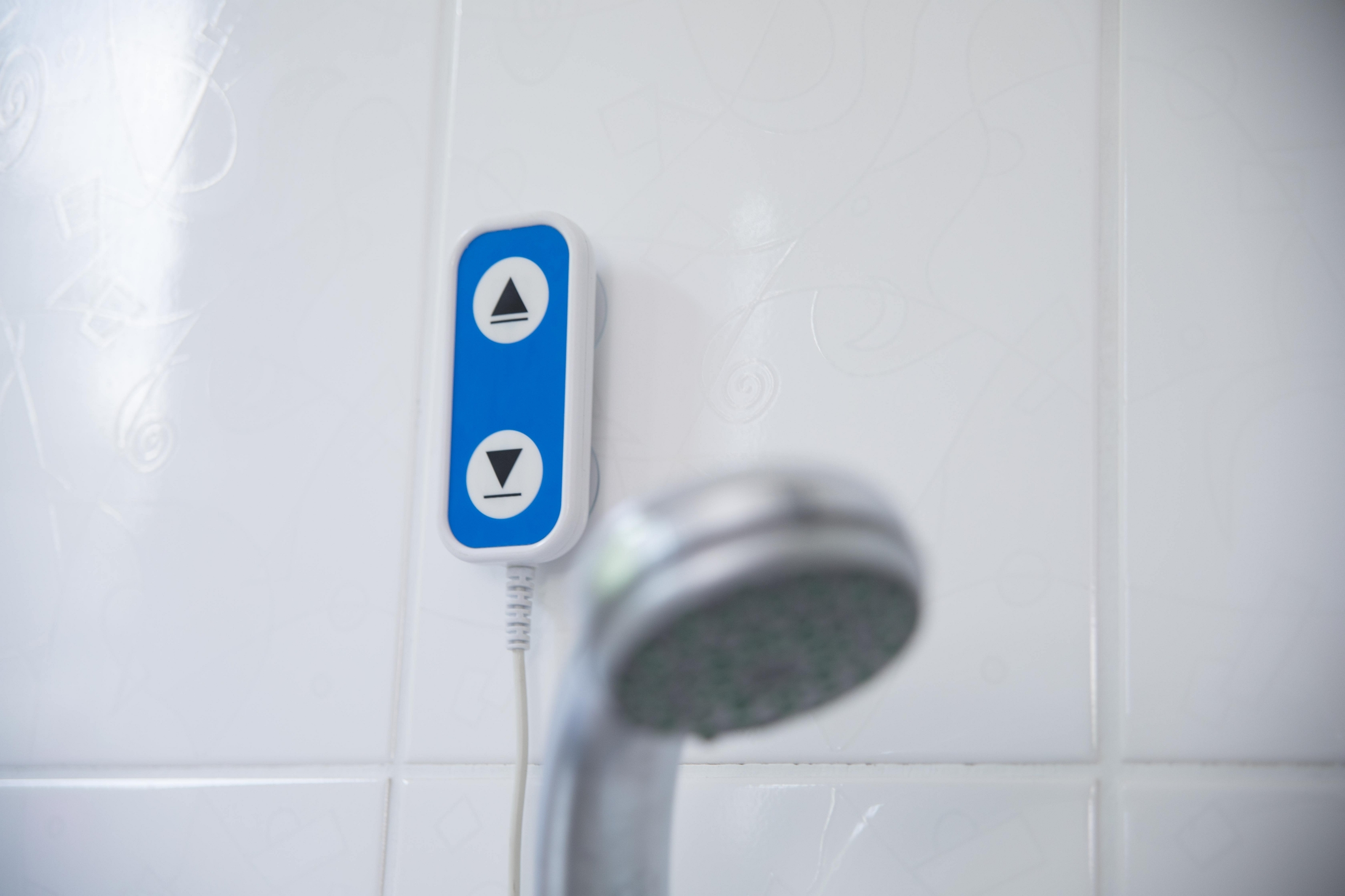 Blau-weißes Duschbedienfeld an einer weiß gefliesten Wand und ein Duschkopf.