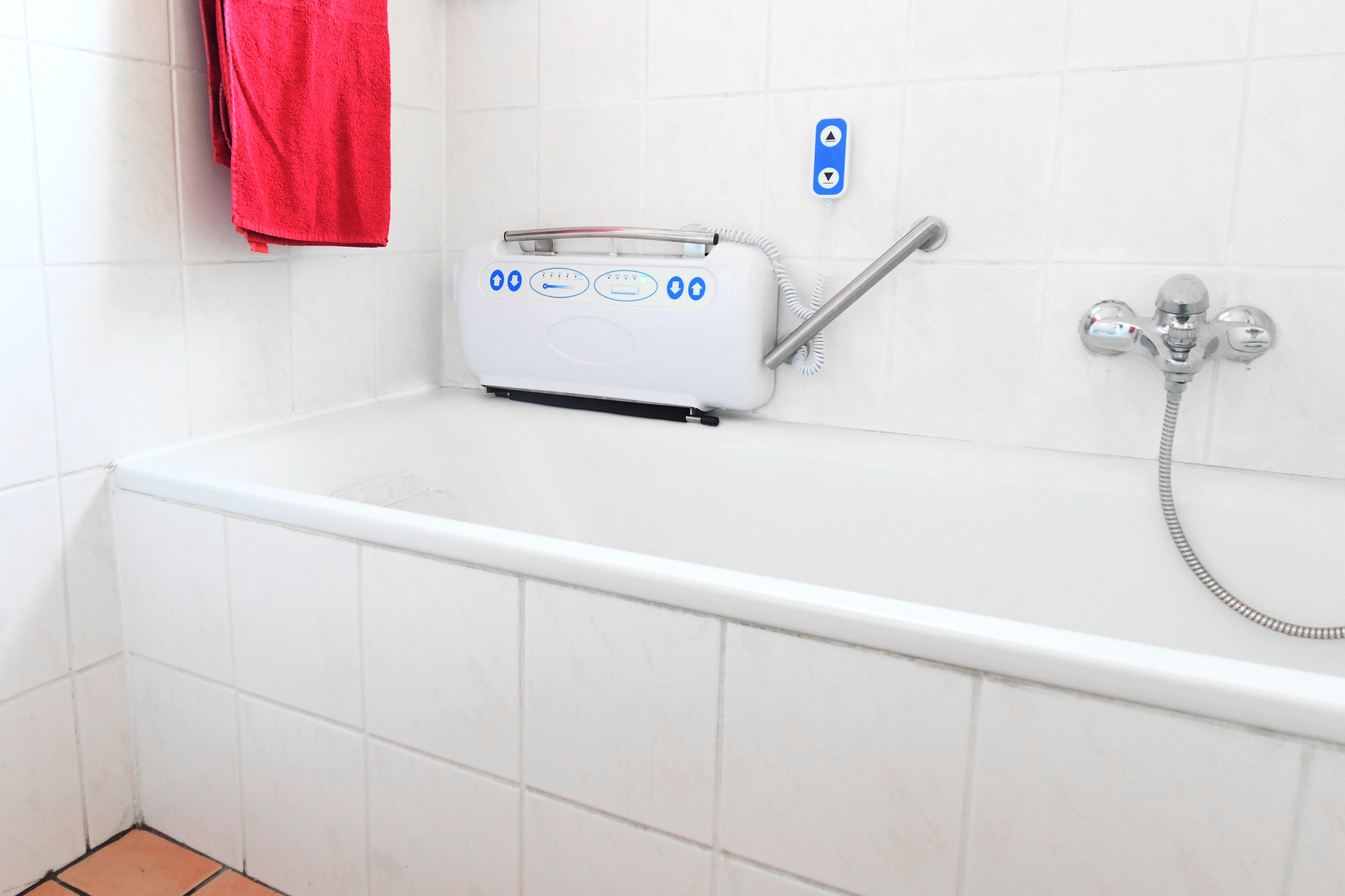Weißes Badezimmer mit Badewanne, wandmontiertem Lifter und rotem Handtuch.