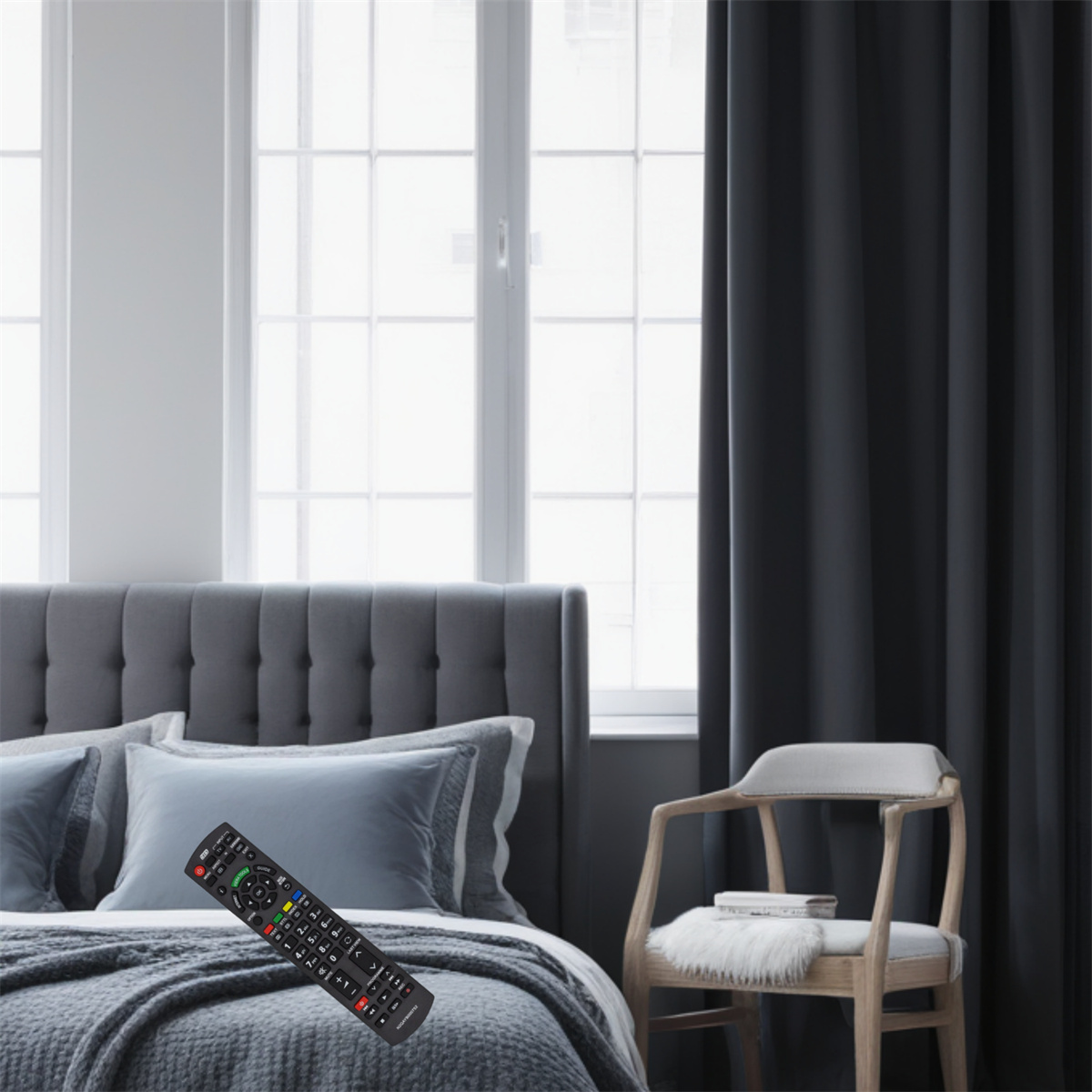 Schlafzimmer mit Bett, Fernbedienung, Fenster, Vorhängen und Stuhl. Die Fernbedienung liegt auf dem Bett.