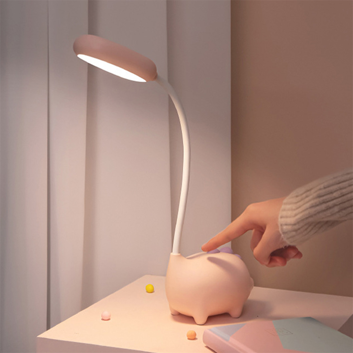 Rosafarbene, schweineförmige Schreibtischlampe mit gebogenem Hals und einer Hand, die den Knopf berührt.