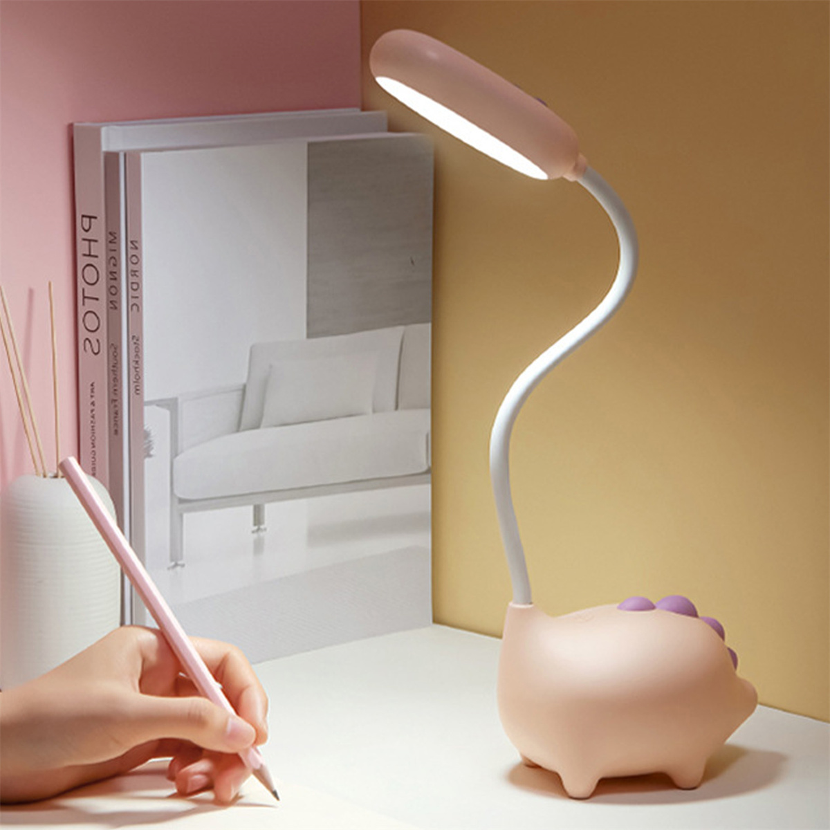 Eine rosa schwein-förmige Schreibtischlampe mit gebogenem Hals und Licht. Hand und Bücher sind sichtbar.