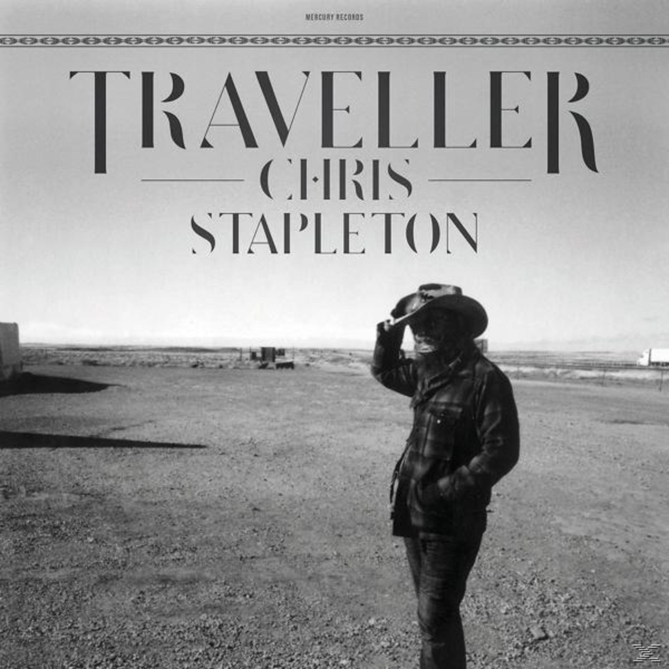 Chris Stapleton, un uomo con un cappello, in piedi su una strada sterrata. Il cielo è nuvoloso.